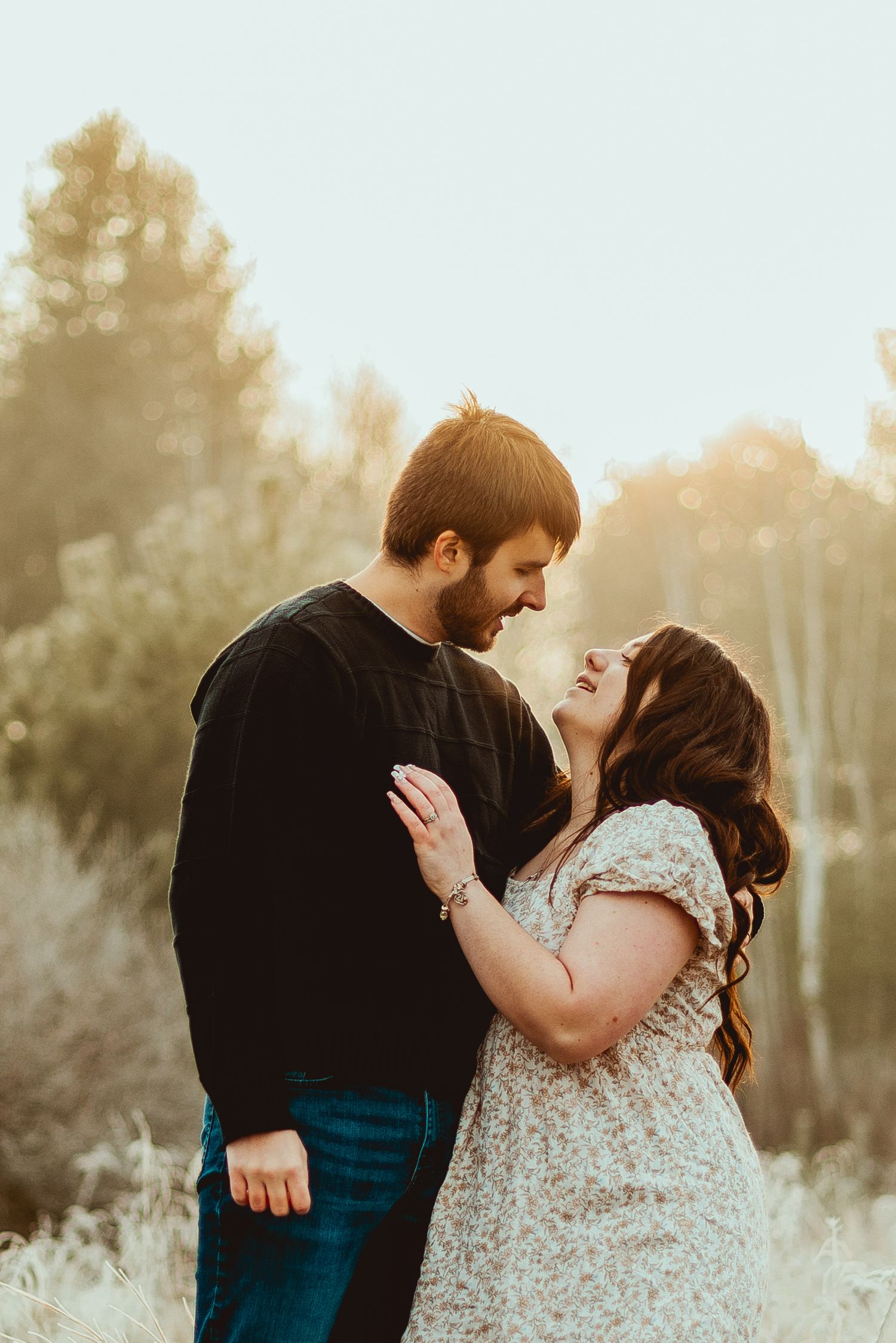 Romantic couple embraces in a sunlit field during golden hour with soft bokeh lighting effects.