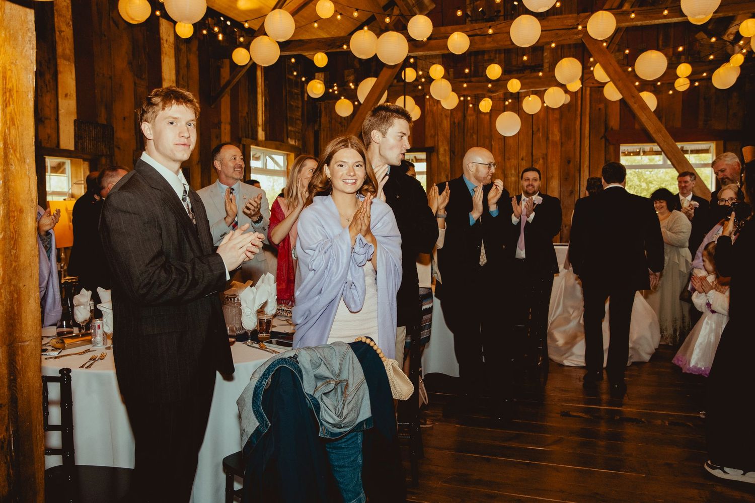 Wedding guests celebrating in warmly lit rustic barn venue decorated with hanging paper lanterns.
