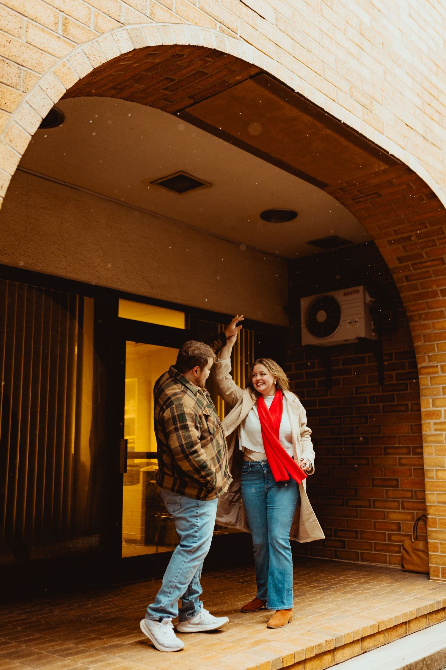 A couple in overalls stands in a brick archway, creating a playful series of progressive poses in warm lighting.