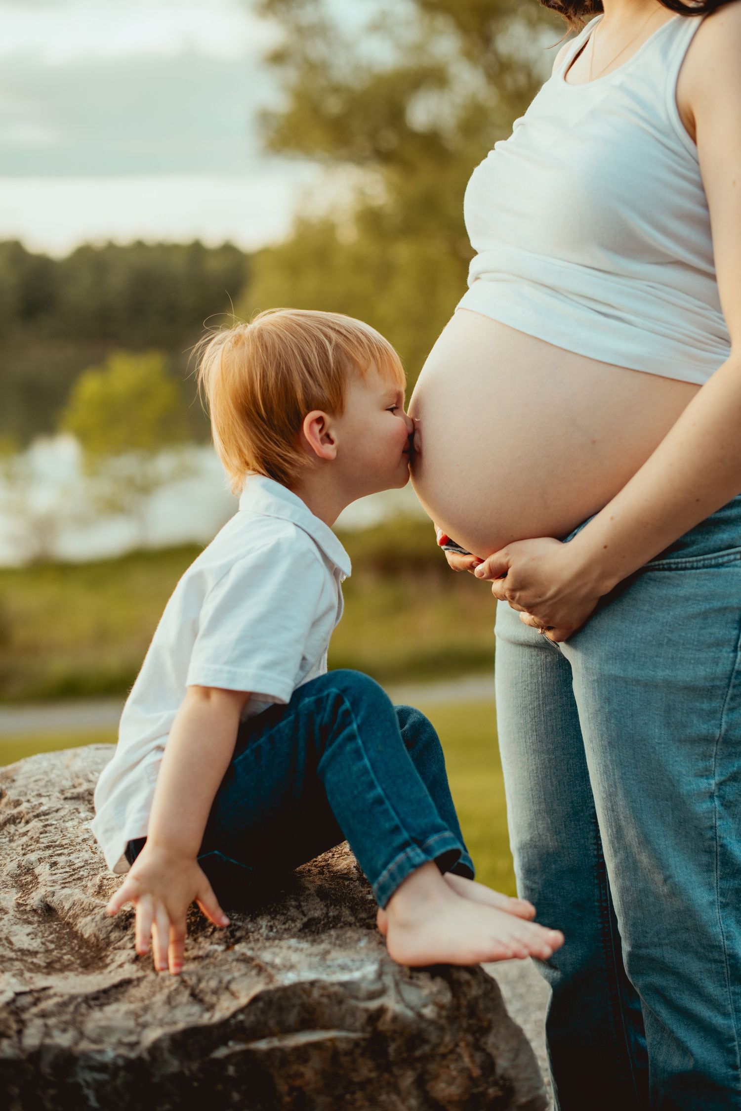 A tender moment captured between a small child and an expectant mother sitting on a rock outdoors.