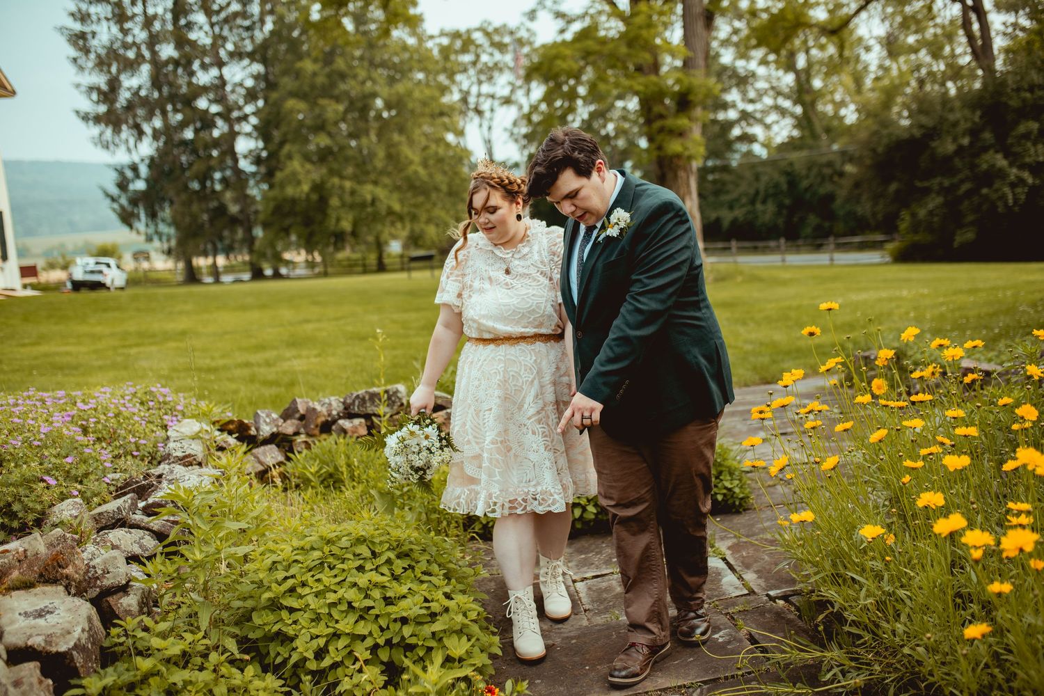 Two people walk along a garden path surrounded by blooming yellow flowers and lush greenery.