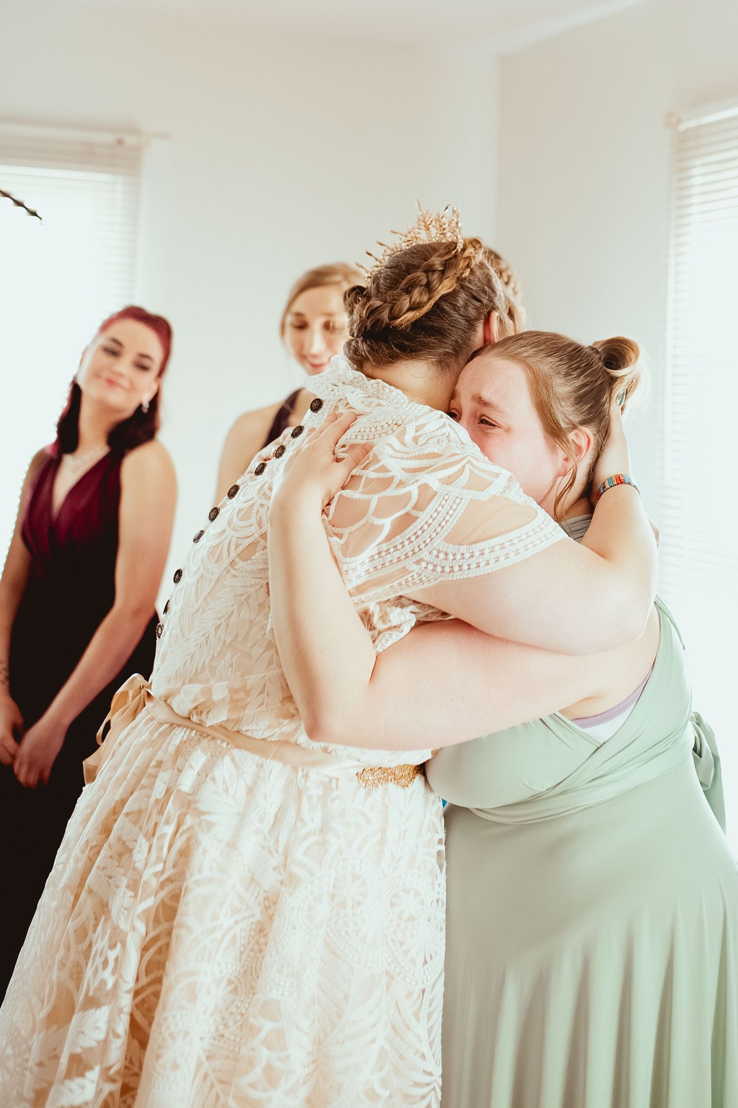 A touching moment between wedding party members wearing pastel bridesmaid dresses and white lace.