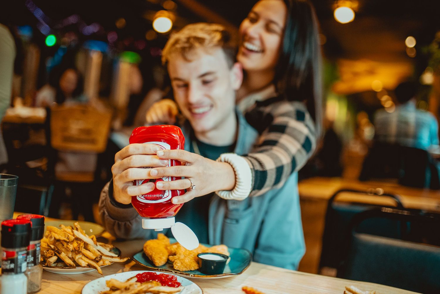 Two people enjoying a casual dinner at a restaurant with french fries and drinks in a warm ambient setting.