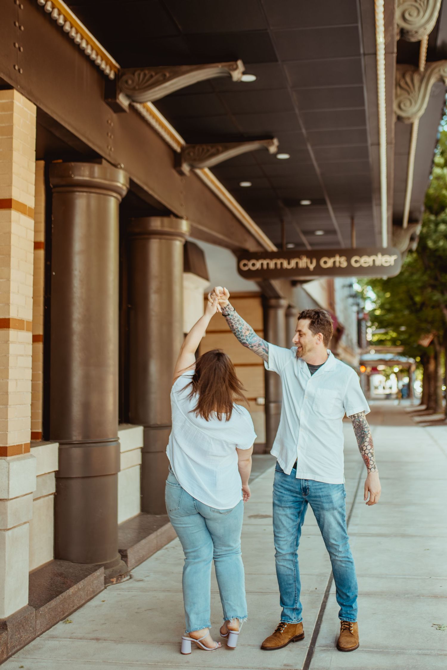 Couple dancing and holding hands outside a Community Arts Center, both wearing white shirts and jeans.