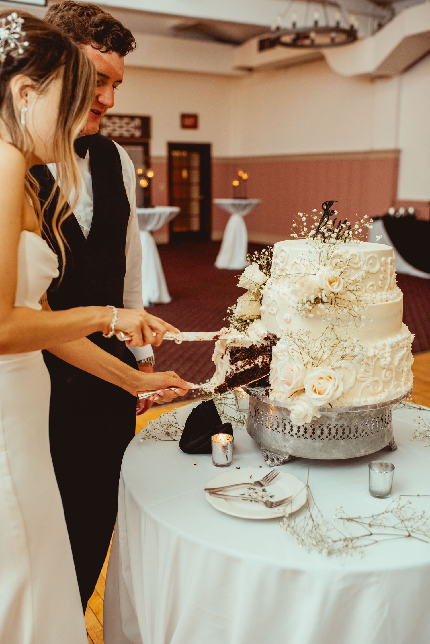 Elegant white wedding cake being cut on a silver platter at the reception.