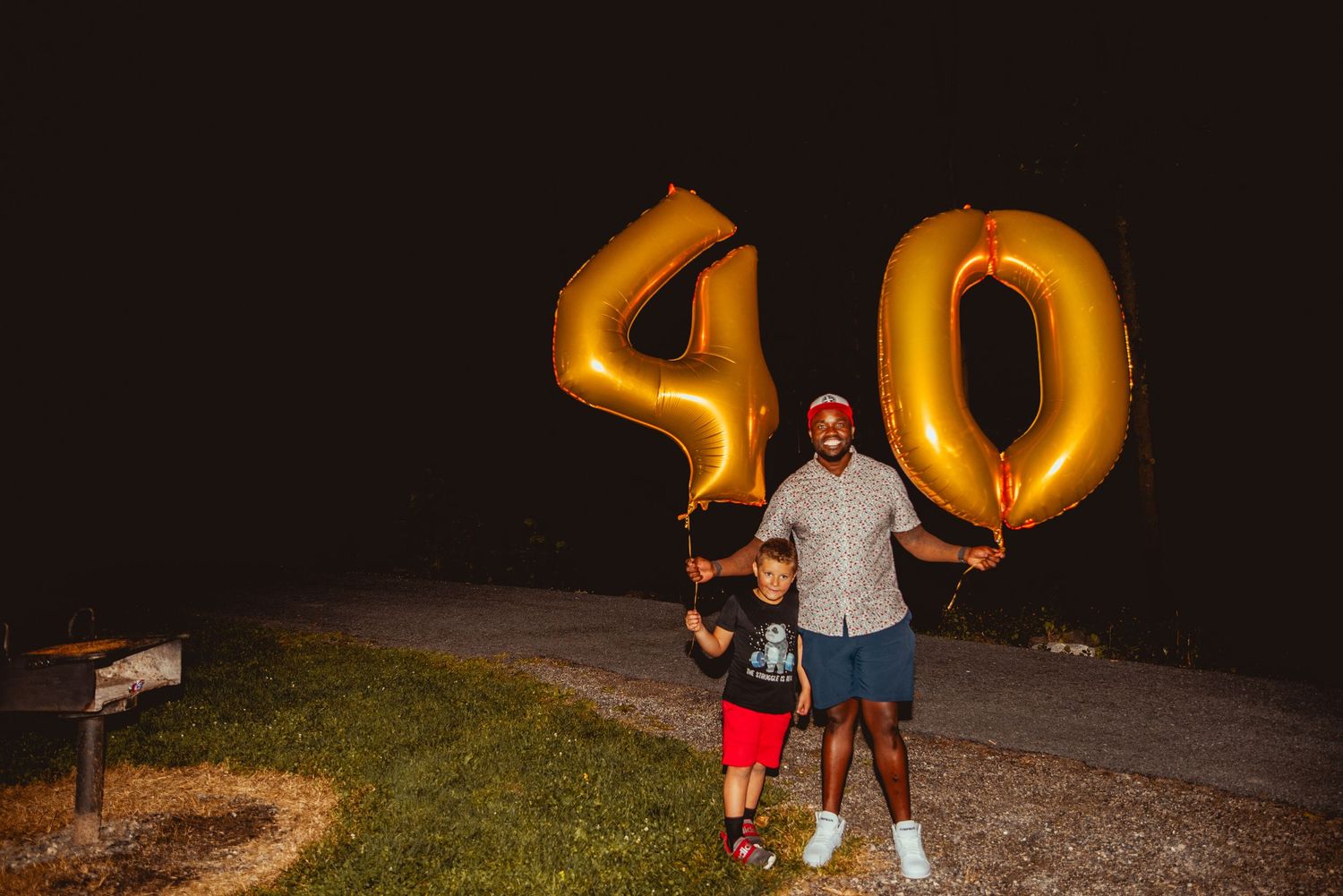 People stand next to illuminated number 50 balloons glowing against dark night sky at outdoor celebration.