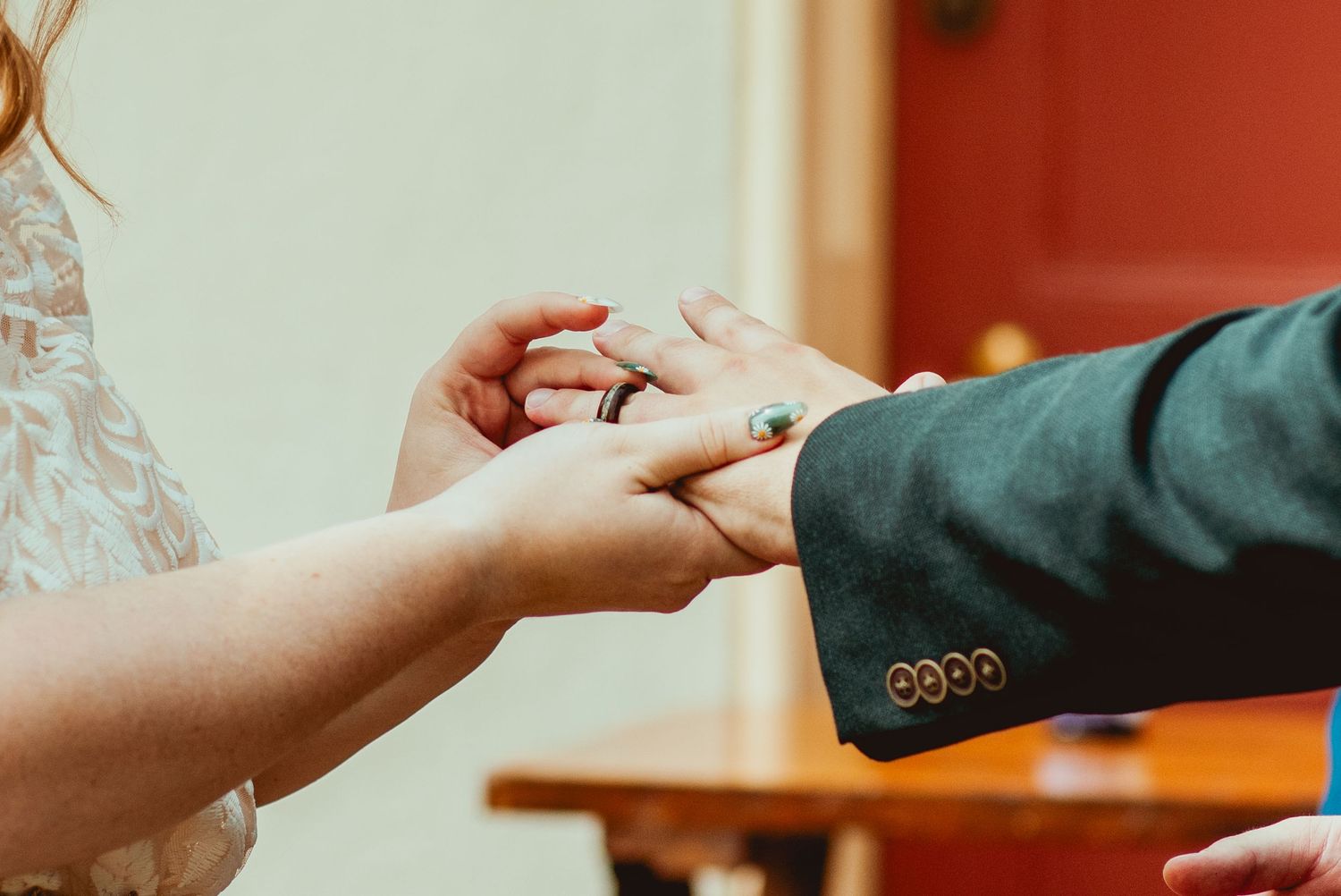 A couple's hands exchanging wedding rings during a traditional ceremony in a warm-lit setting.
