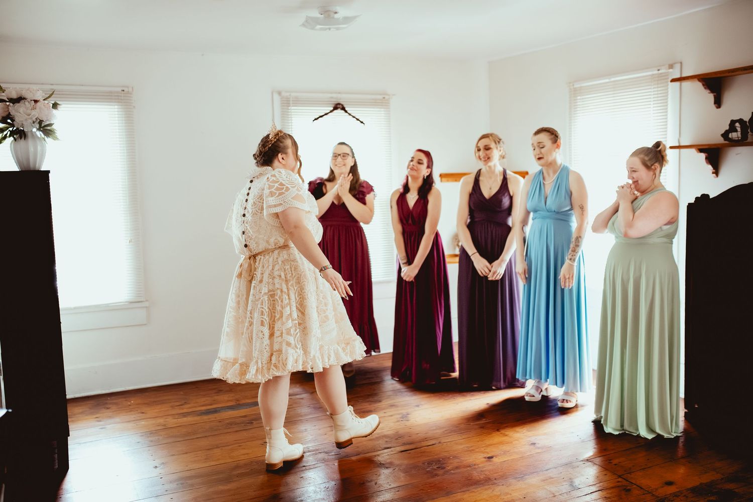 Wedding party members in coordinating burgundy, blue and sage dresses pose together in a bright indoor space.