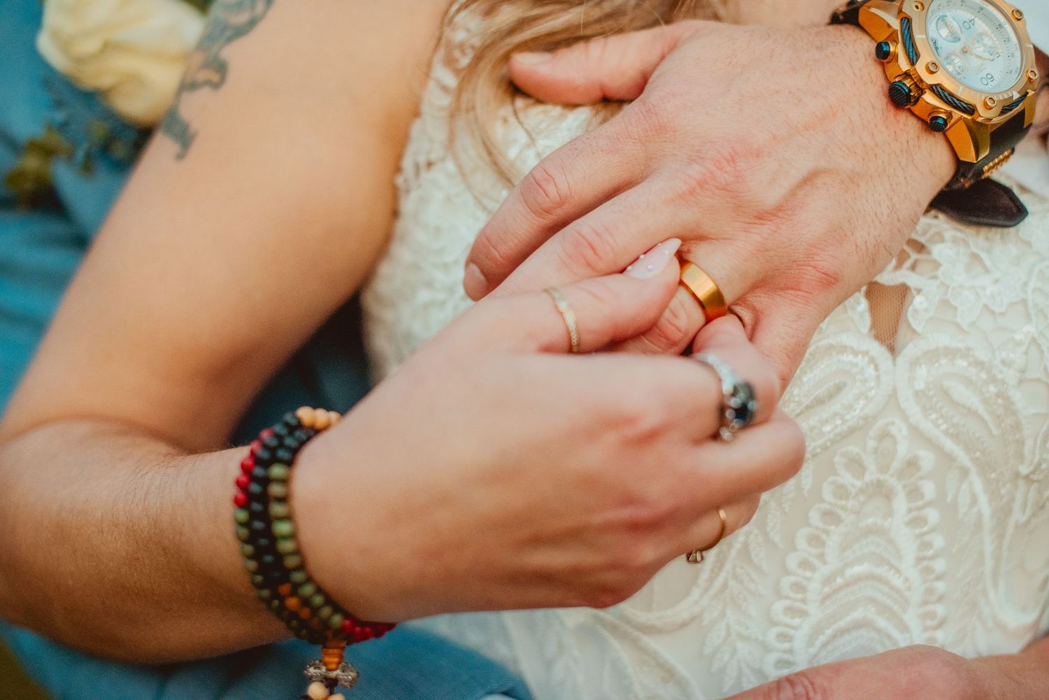 Close-up of hands with wedding rings and jewelry against lace dress fabric.