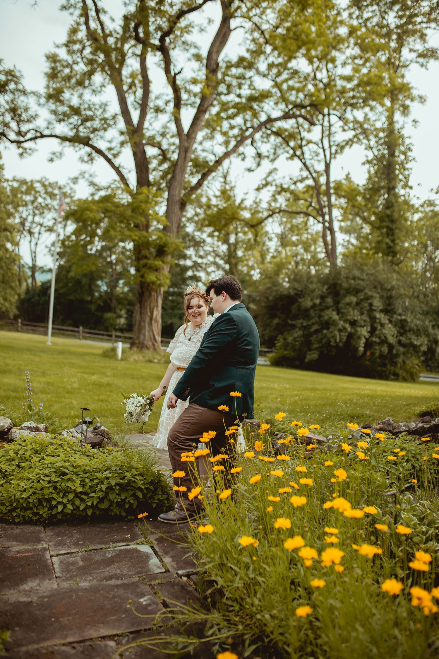 A couple sits together on stone steps surrounded by blooming yellow wildflowers in a garden setting.