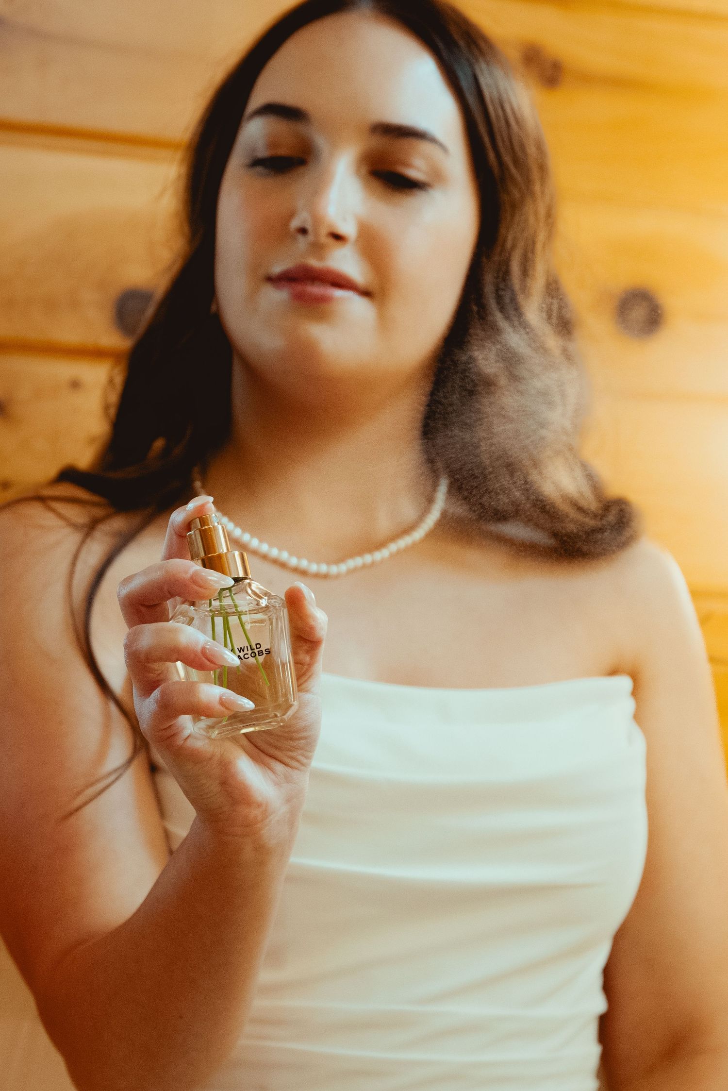 Close-up shots of a woman in white dress holding a perfume bottle and wearing a pearl necklace.