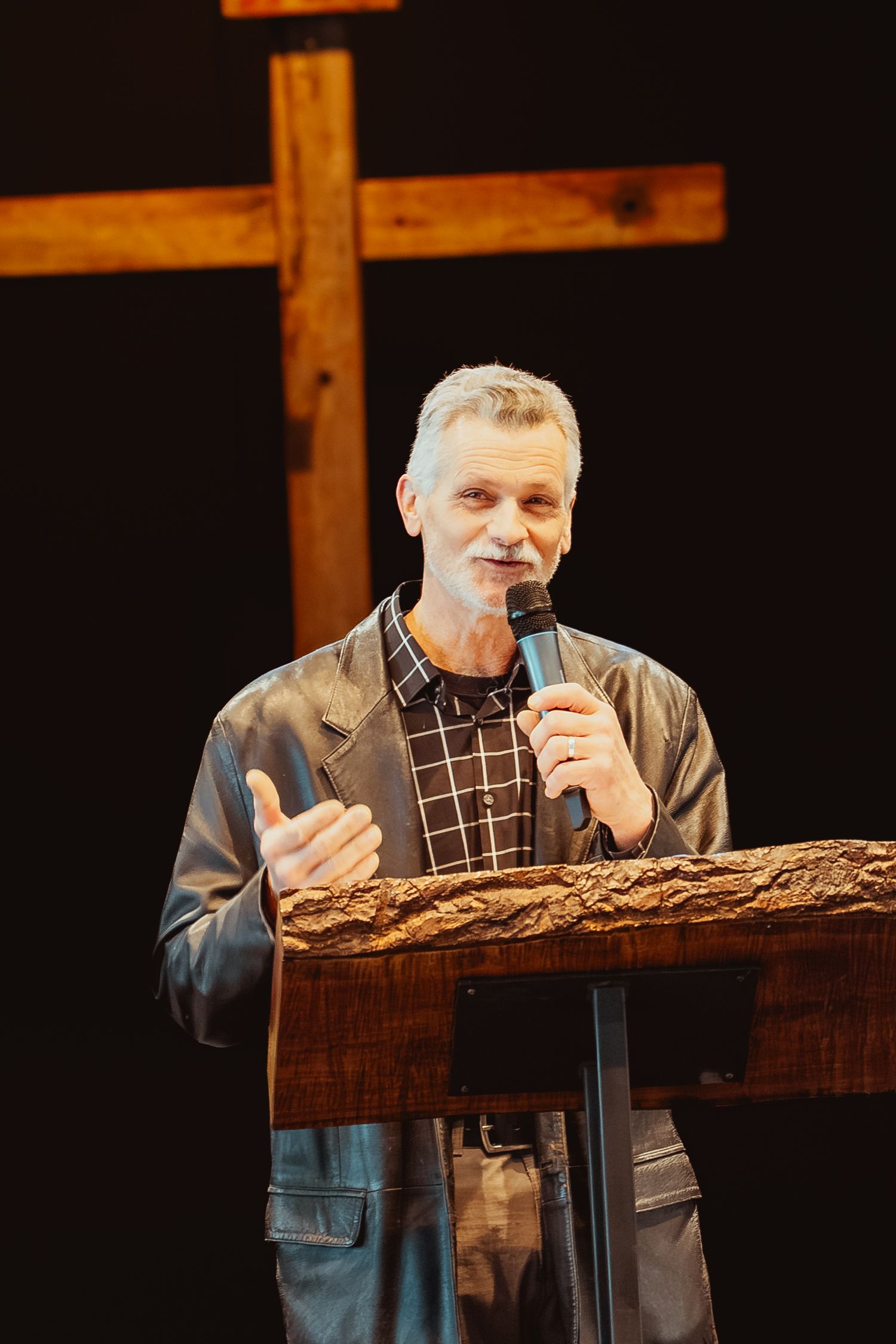 A speaker stands at a wooden podium delivering a presentation in a dimly lit venue.