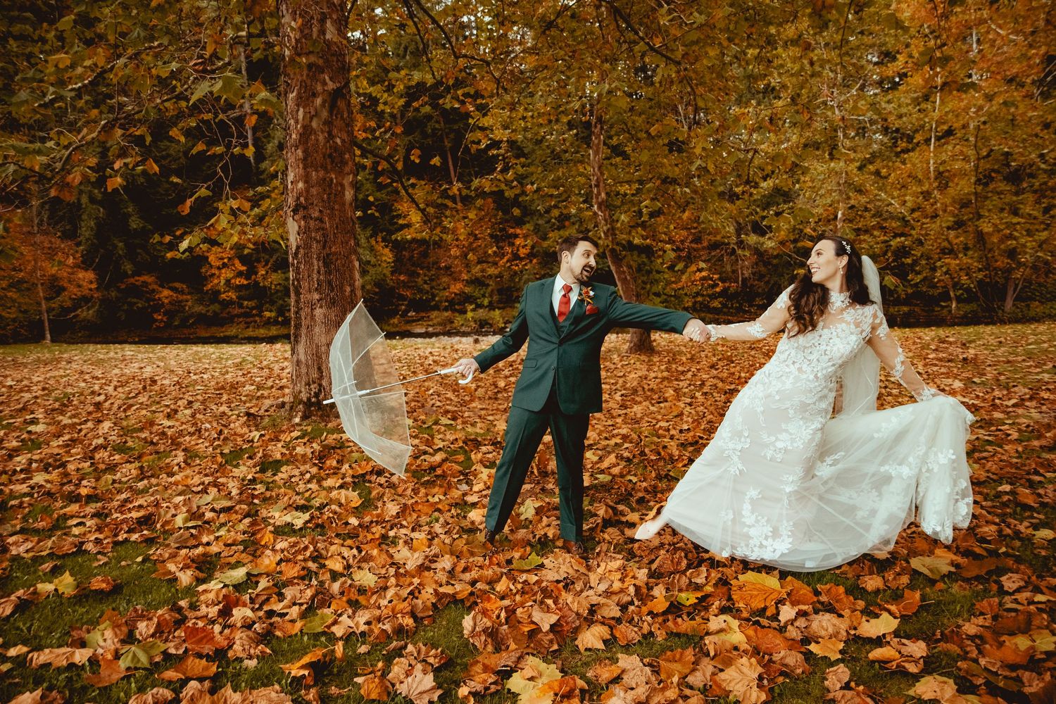 Couple playfully throws autumn leaves in a romantic forest photoshoot wearing wedding attire.
