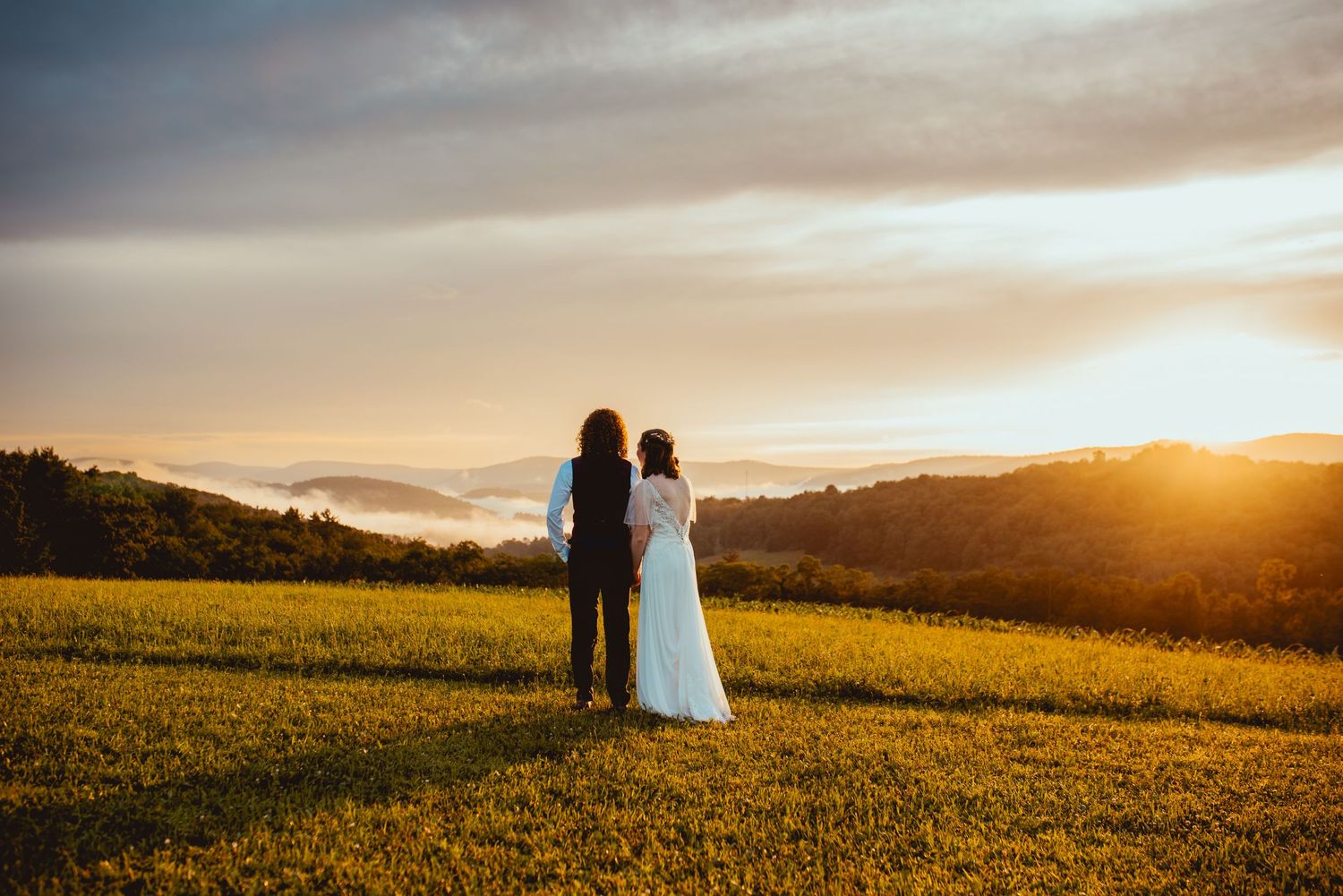 Two figures stand in a golden field at sunset creating silhouettes against the warm glowing sky.