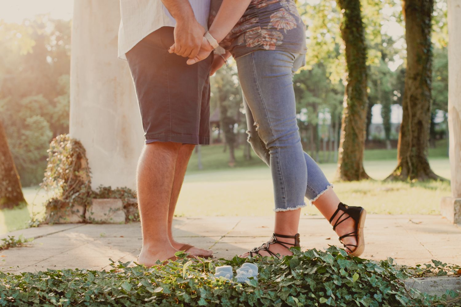 A couple in casual clothing walks together on a sunlit path through a park during golden hour.