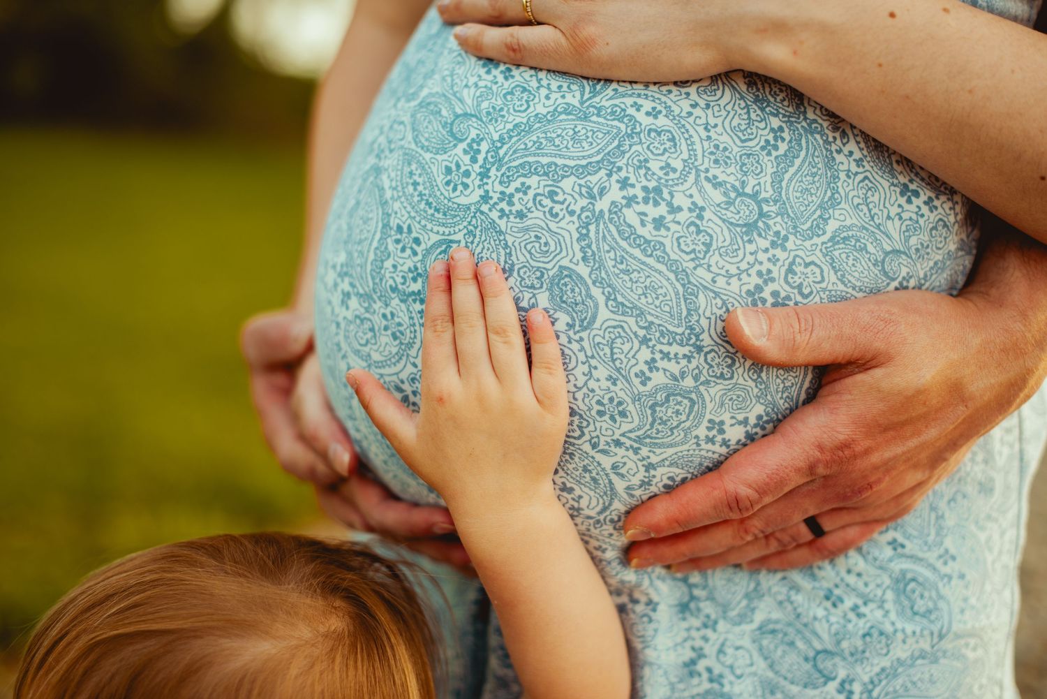Hands gently touch a light blue lace maternity dress fabric showing the progression of a growing baby bump.