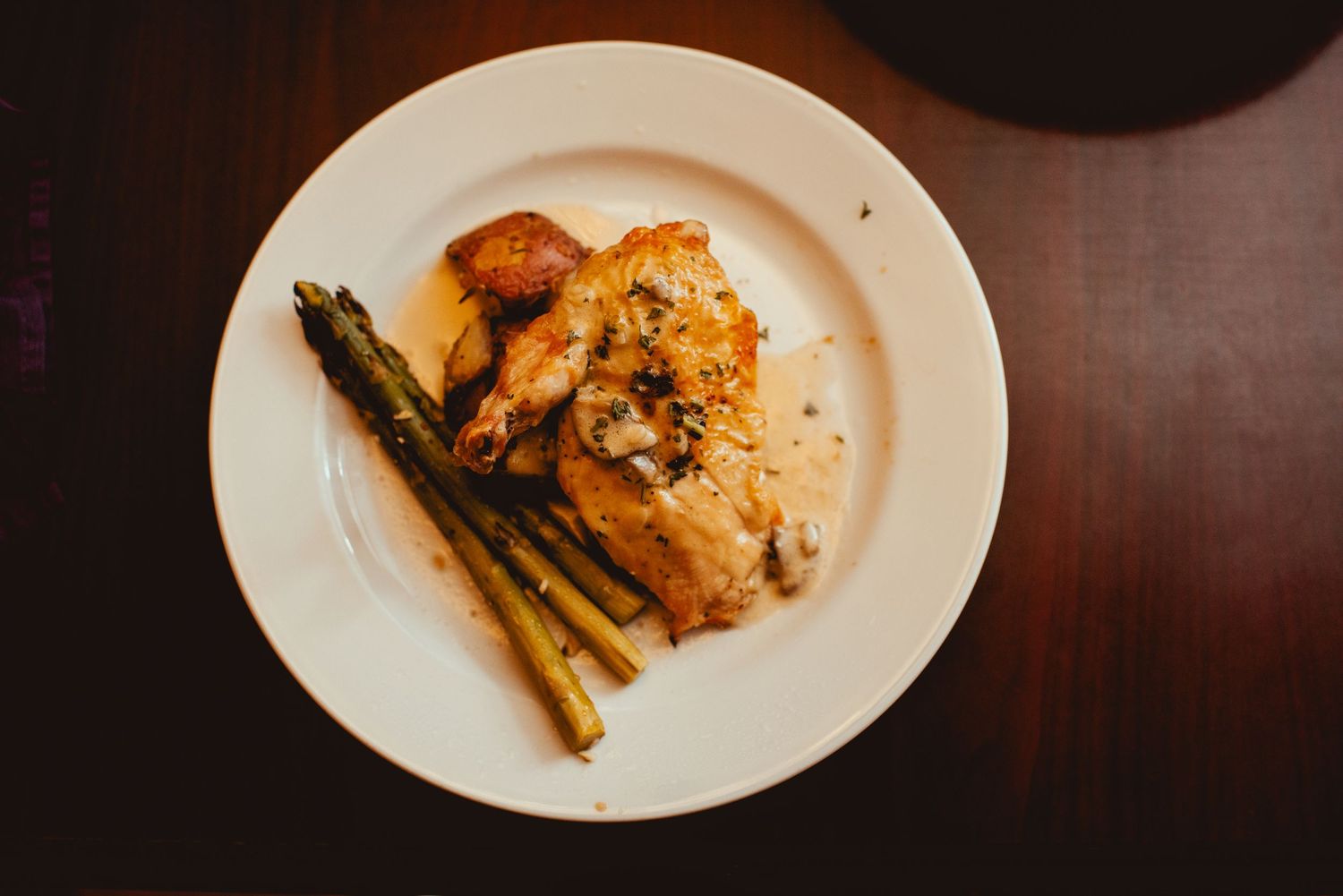Elegant plated dinner dishes with asparagus and protein on white plates against dark wood table.