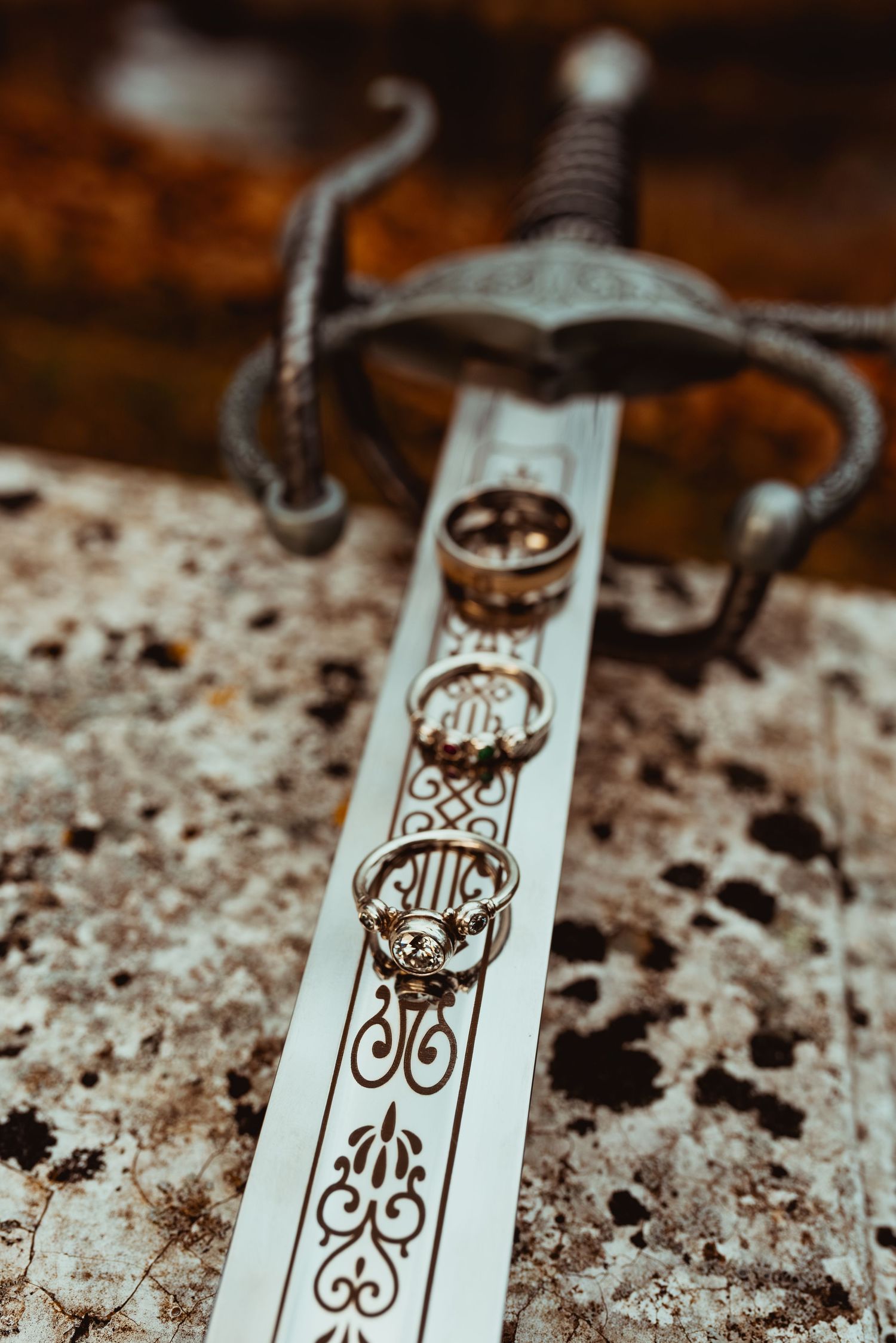 Close-up view of an ornate sword blade with intricate decorative patterns and wedding rings placed on its surface.