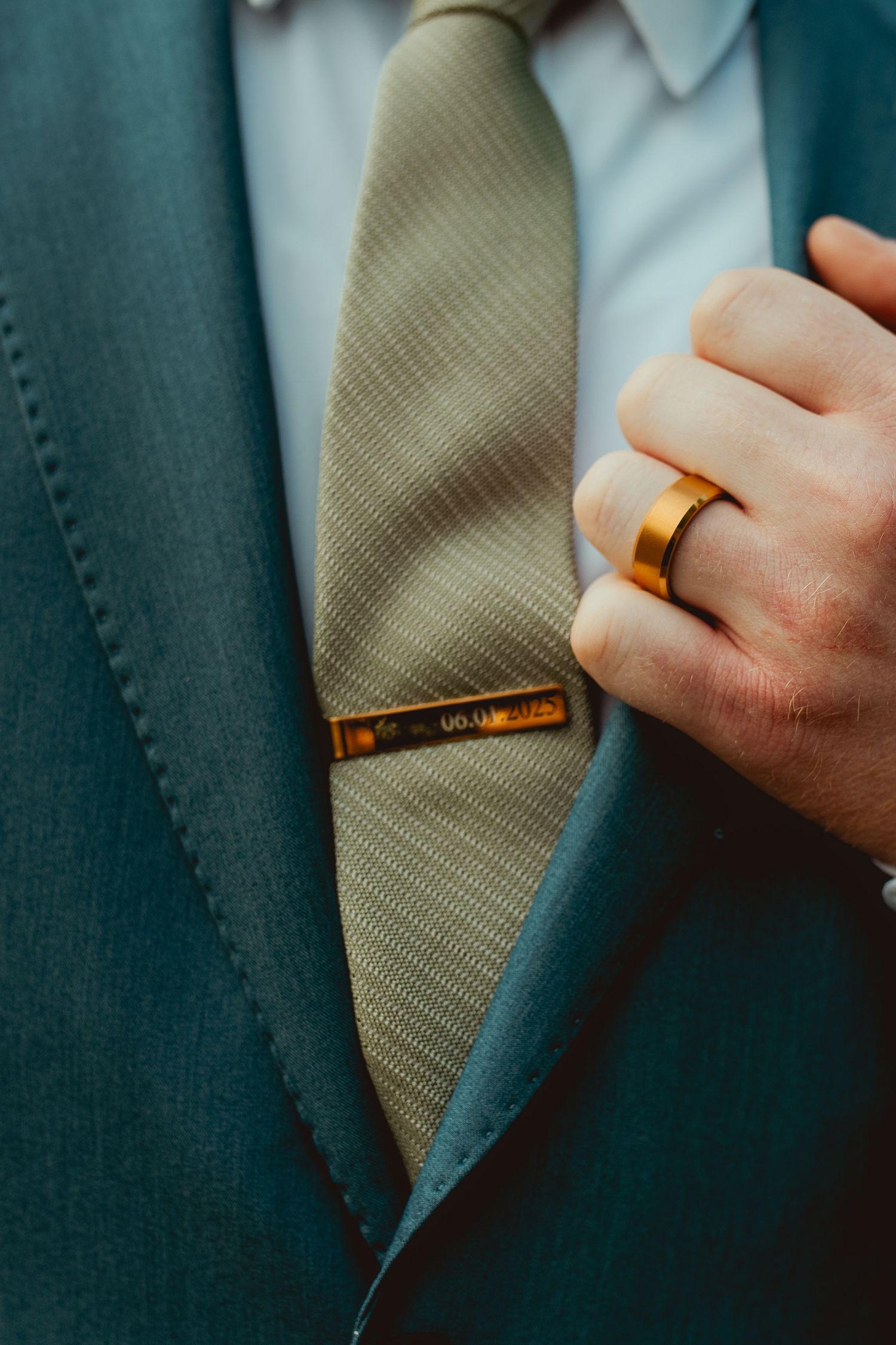 Detail shot of teal suit with tie clip and gold wedding band.