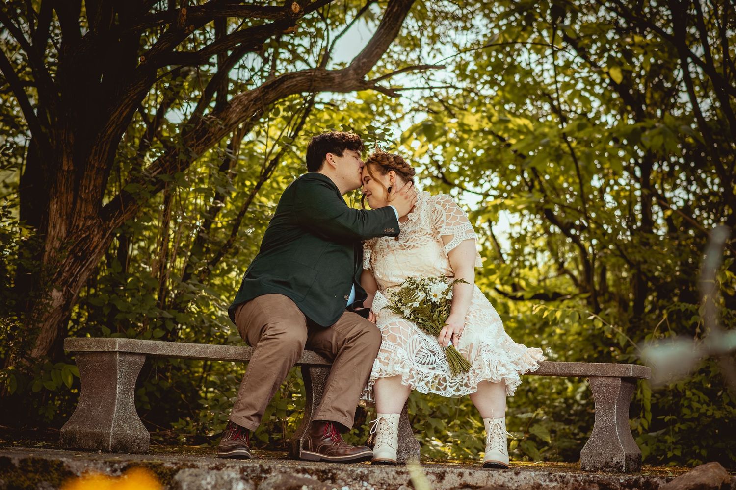A romantic moment captured on a stone bench in a sunlit garden with golden autumn trees in the background.