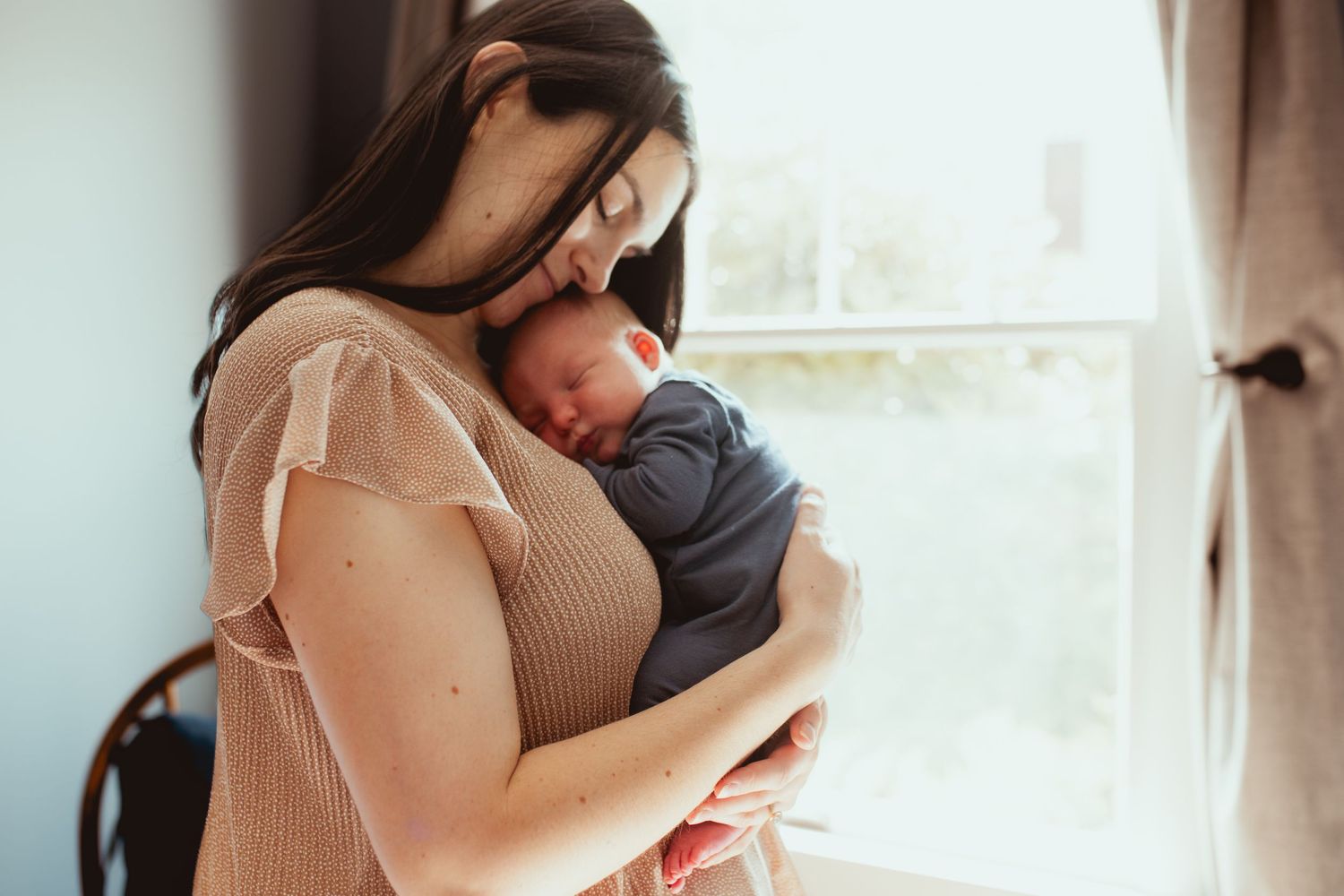 A romantic couple embraces intimately in soft window light during a tender moment together.