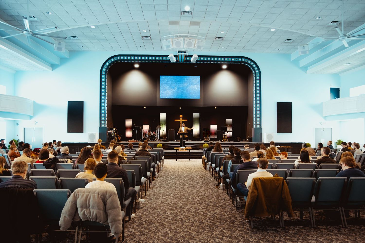 Interior view of a modern church auditorium with rows of seats and a stage with screens and lighting.