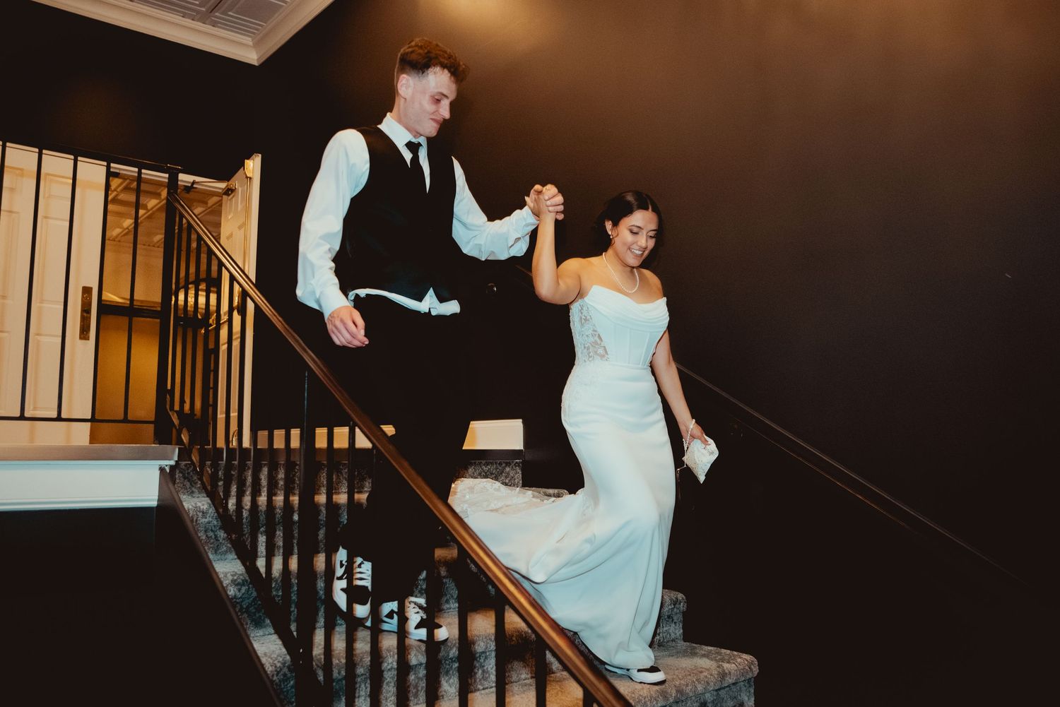 Bride in white dress and wedding party members descending an elegant dark staircase.