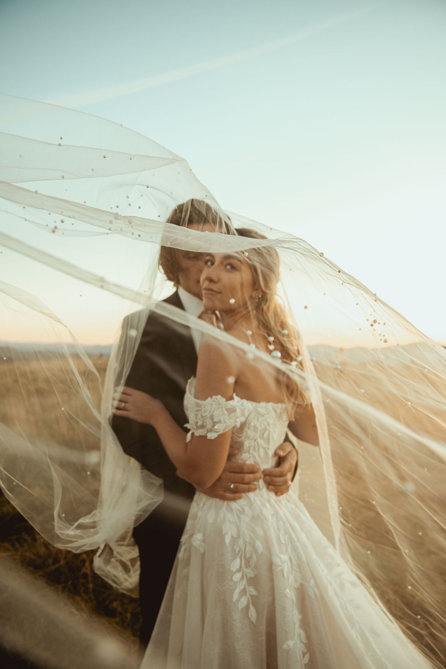 A romantic wedding portrait with flowing veil and lace dress details against mountain scenery.