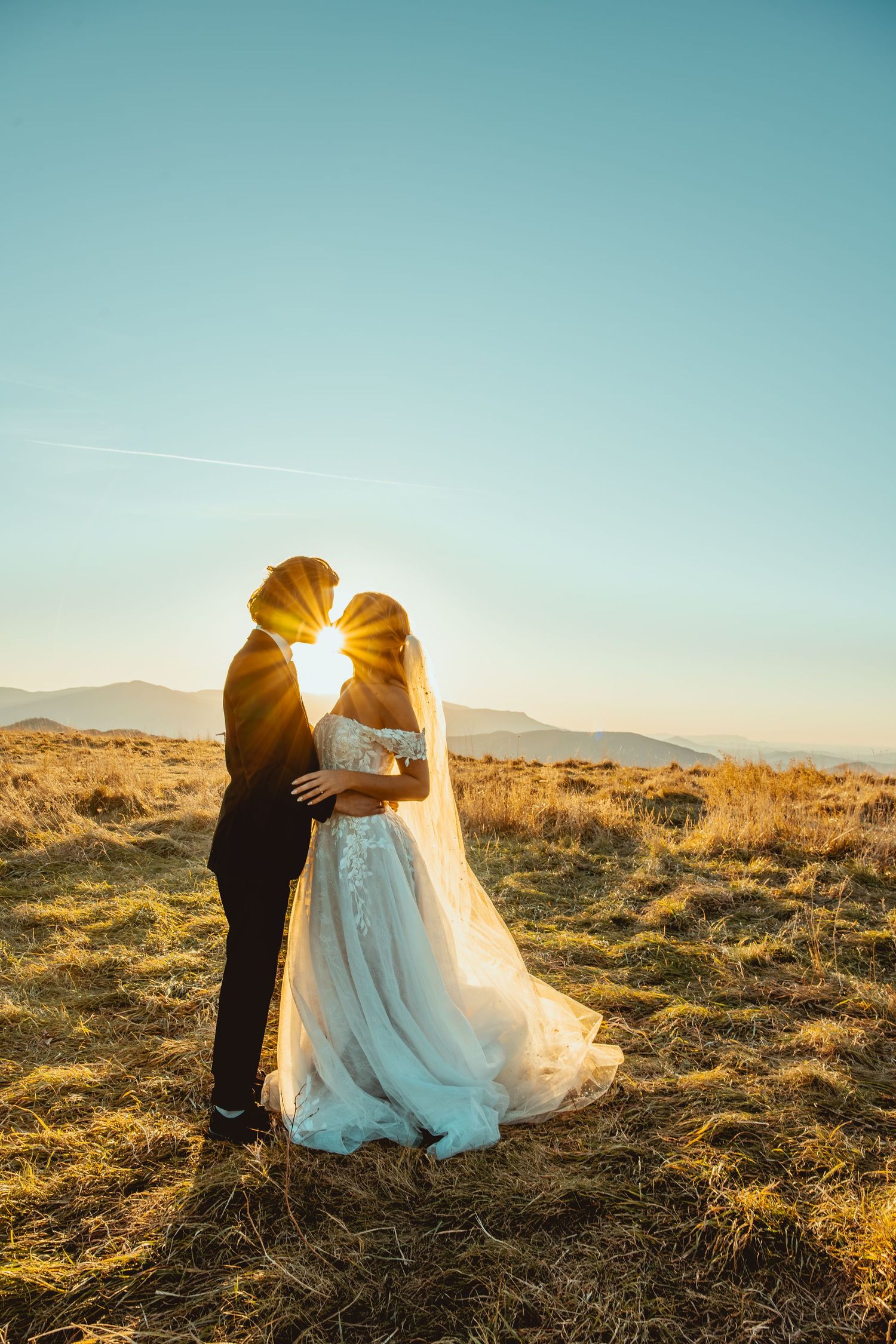 Sunset wedding portrait with couple embracing in golden light on mountain landscape.