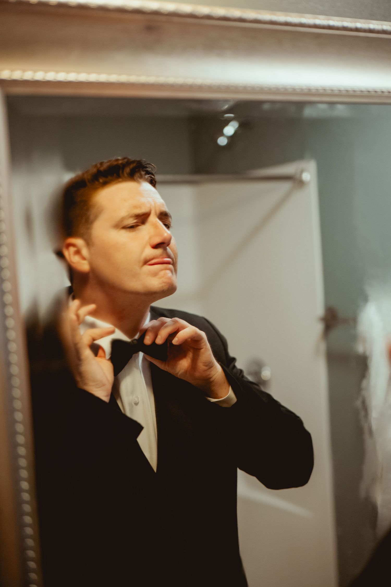 Person adjusting bowtie while getting ready in formal attire for special occasion.