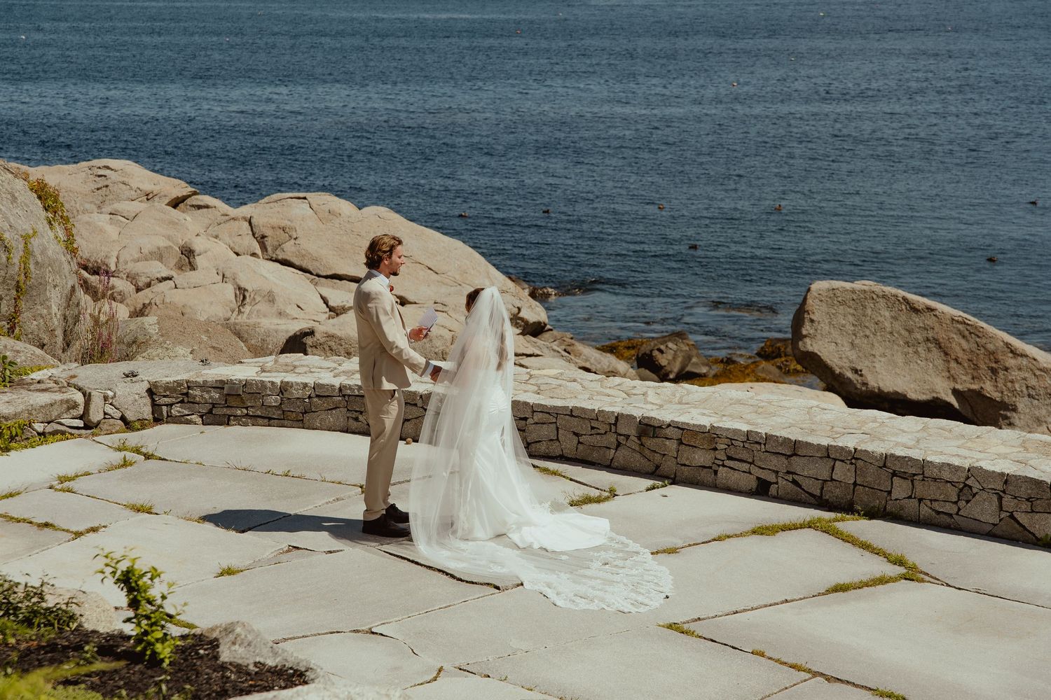 Bride and groom share a romantic first look on rocky coastal stone patio with ocean views on their wedding day.