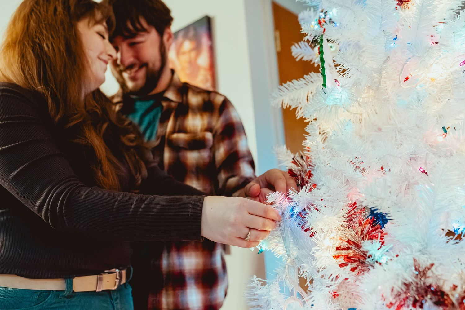A couple embraces in front of a white wall with red and blue paint splatters creating an artistic backdrop.