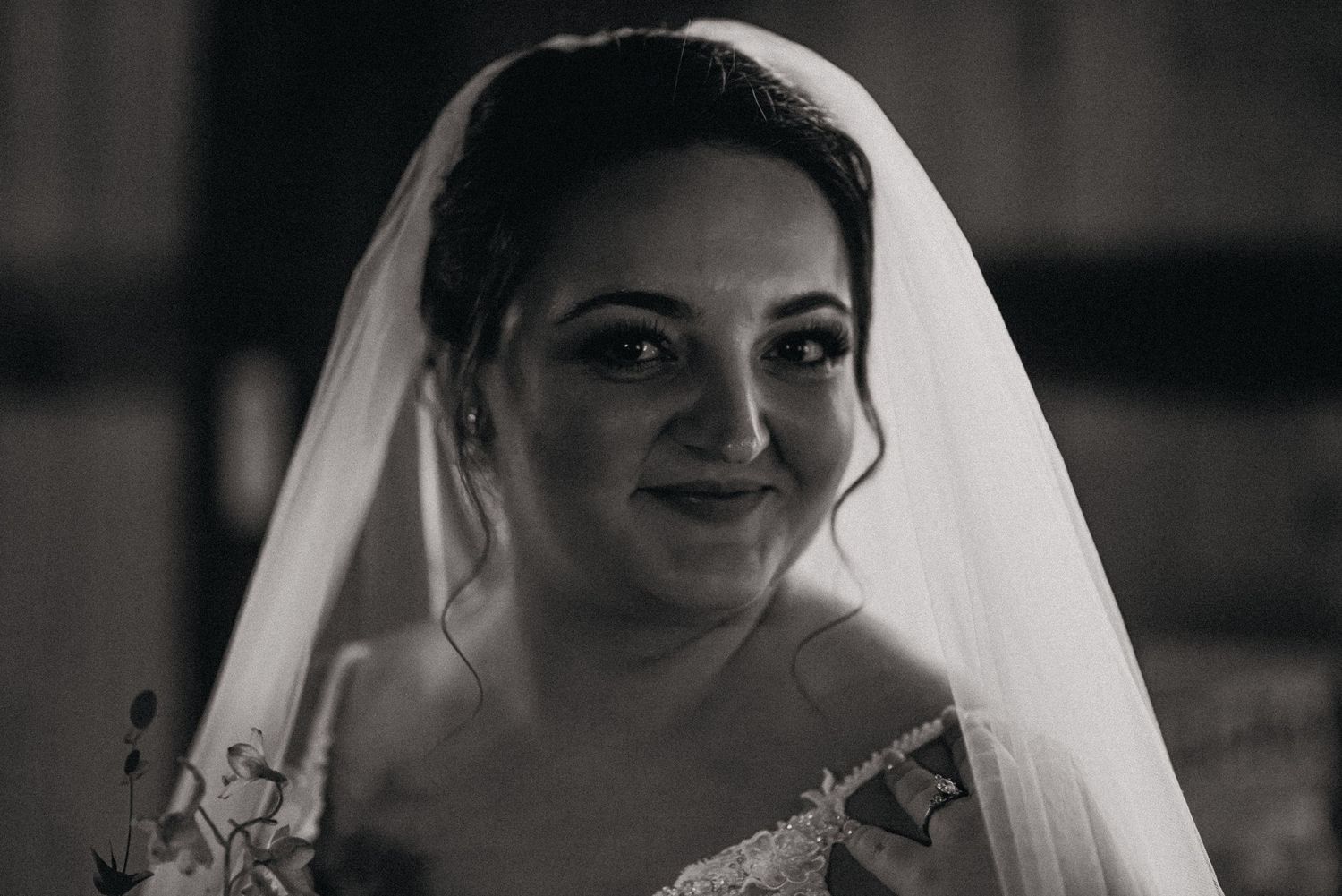 Black and white portrait of a smiling bride wearing a veil and lace wedding dress on her wedding day.