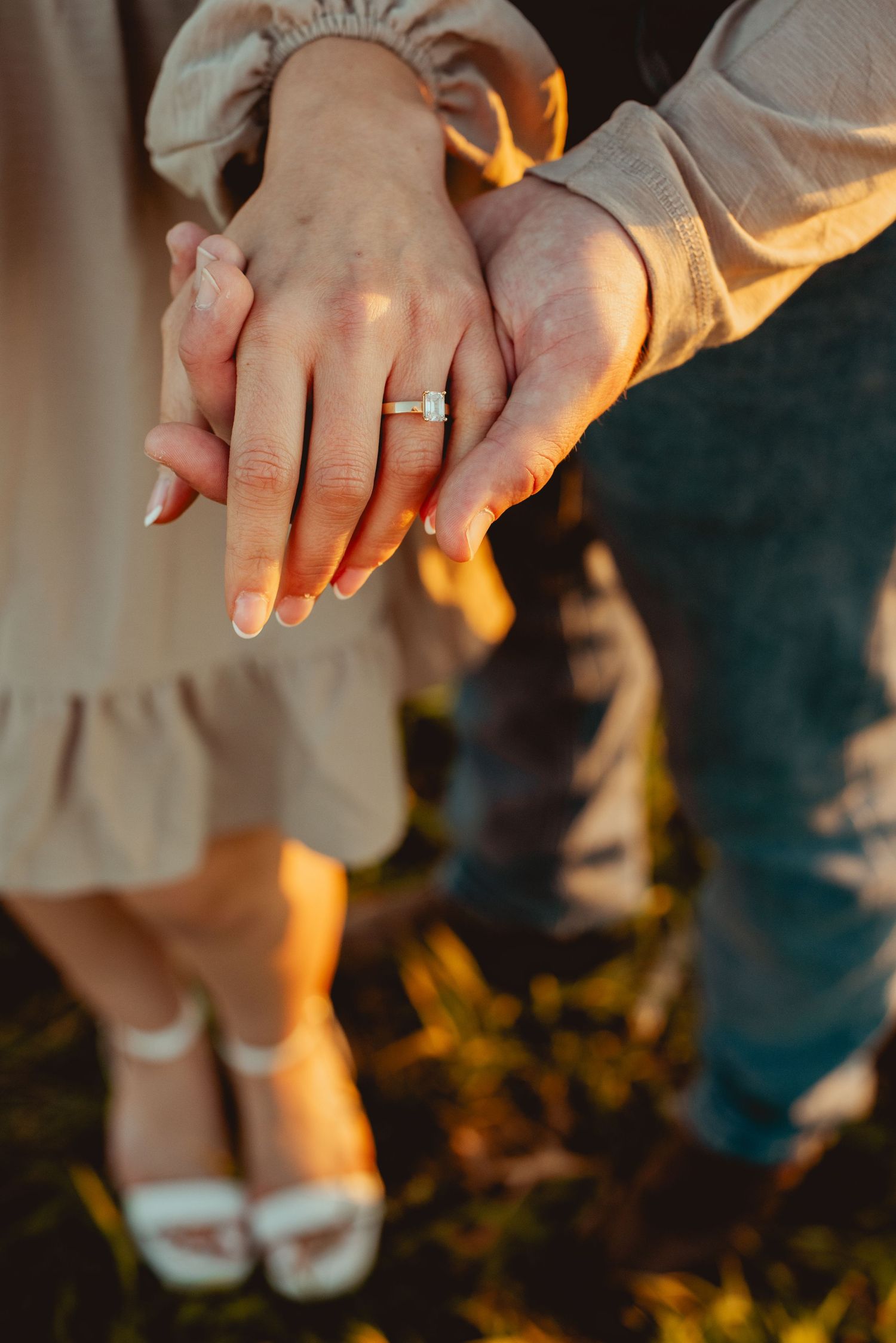 Close-up of hands wearing wedding rings with warm sunset lighting filtering through trees in the background.