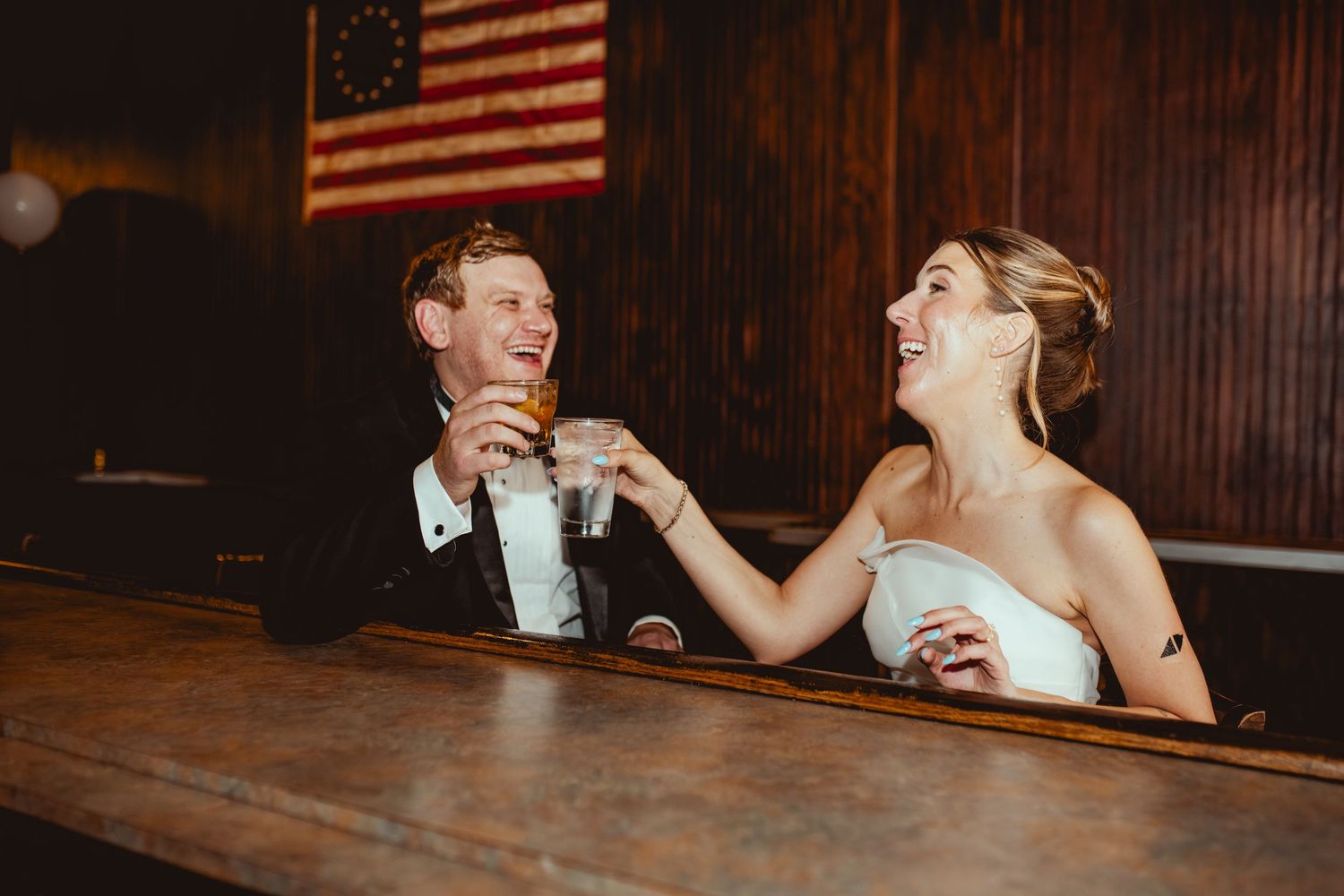 Wedding reception in rustic venue with American flag displayed on wood-paneled wall.
