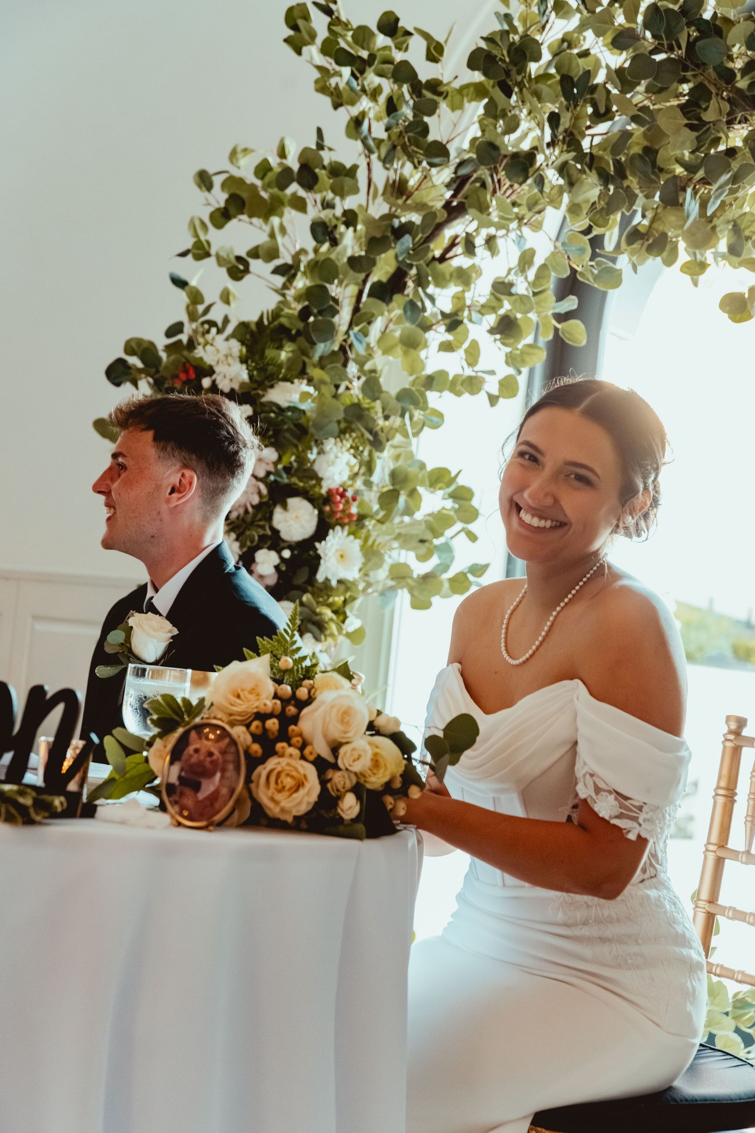 Wedding couple shares a joyful moment near decorative greenery and floral arrangements.