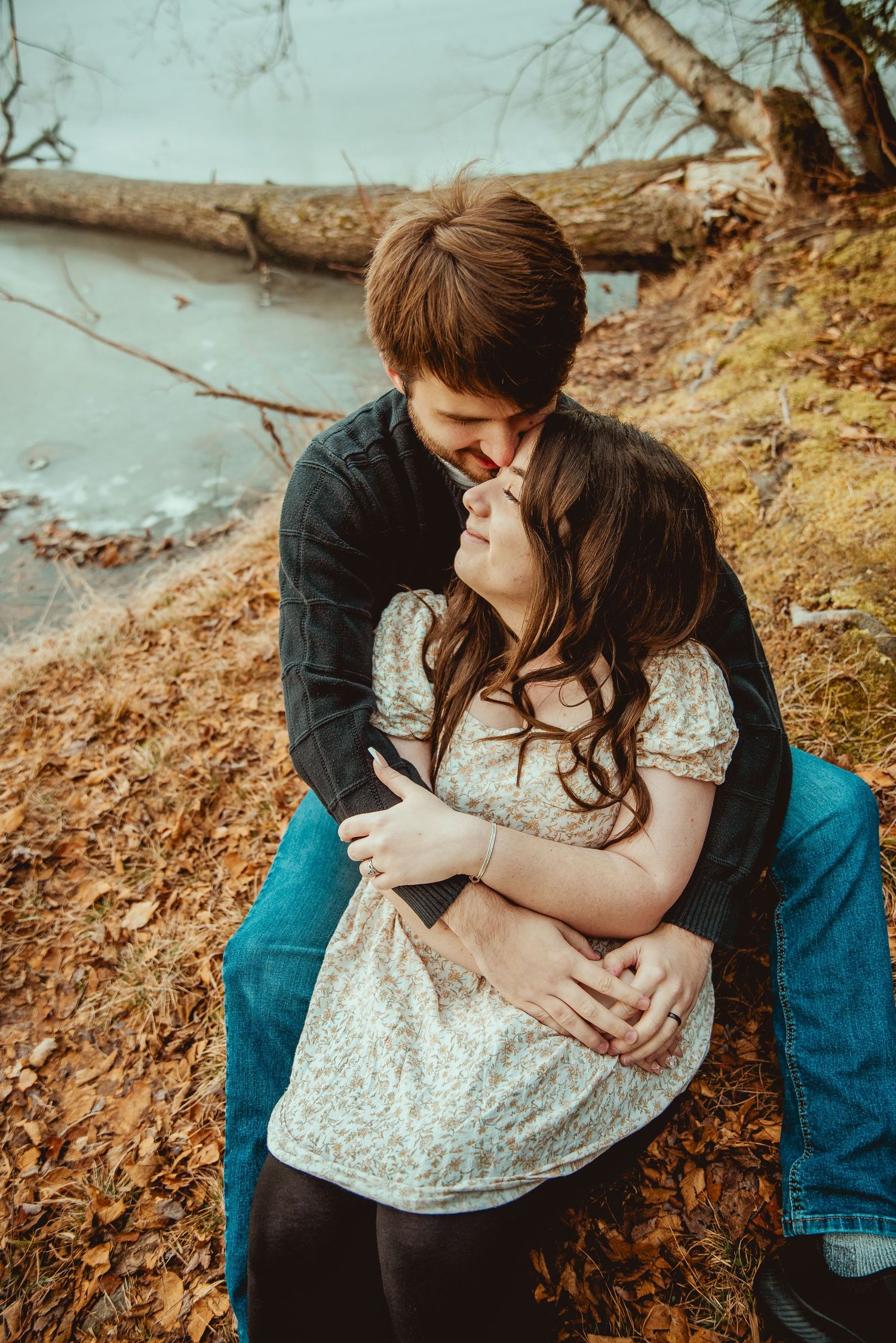 A romantic couple sits together on autumn ground wearing denim and white lace in an intimate outdoor photoshoot.