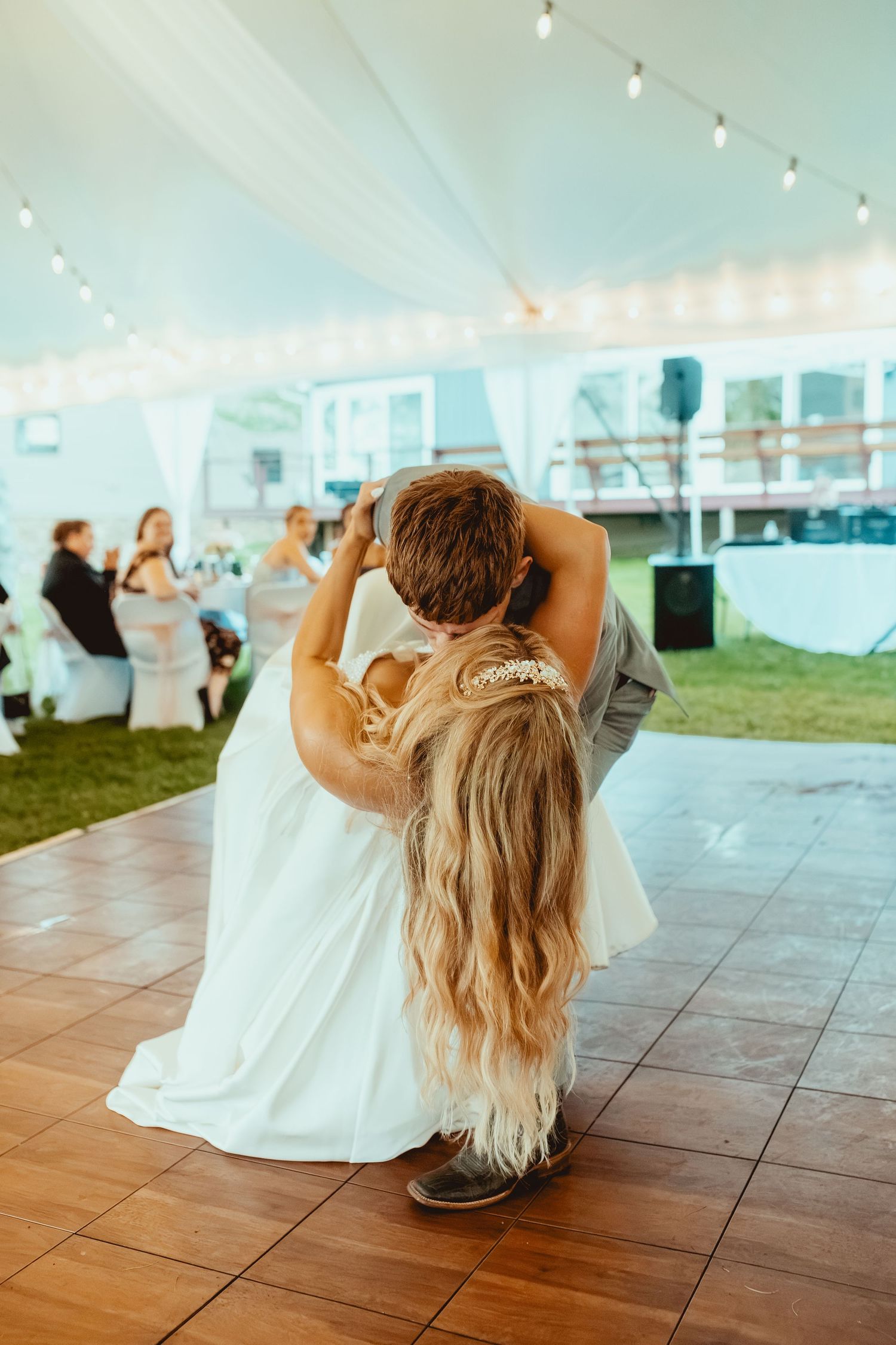 Bride and groom sharing first dance under a tent at outdoor wedding reception on a wooden dance floor.