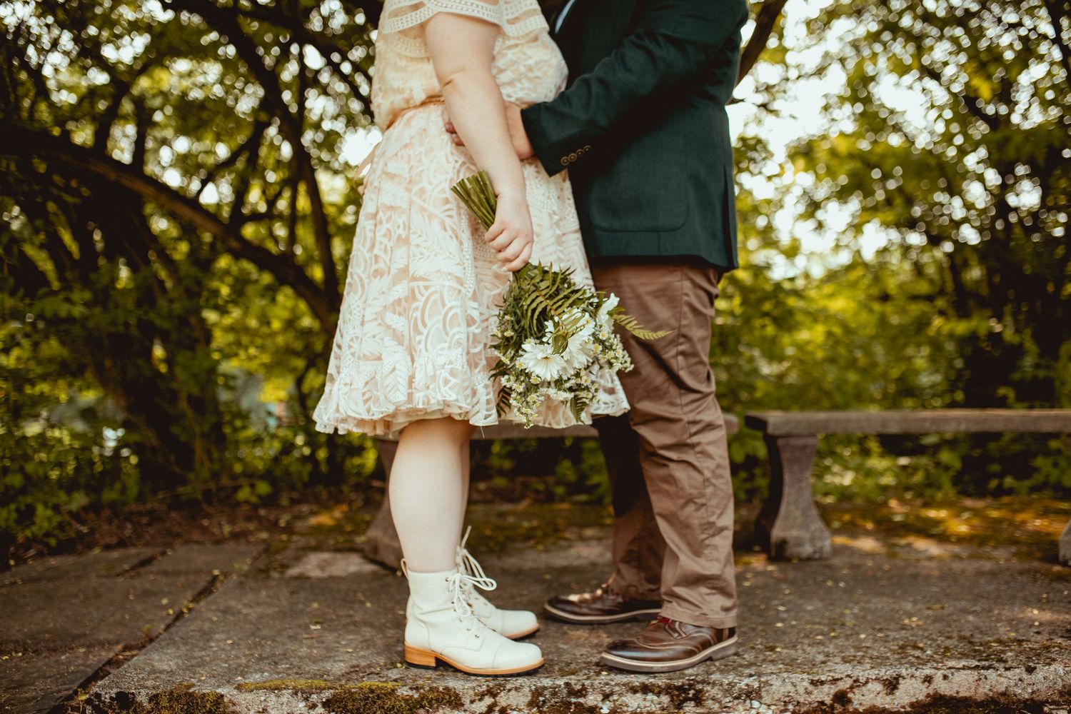 Close-up of feet showing white cowboy boots and brown shoes standing together on a dirt path in nature.