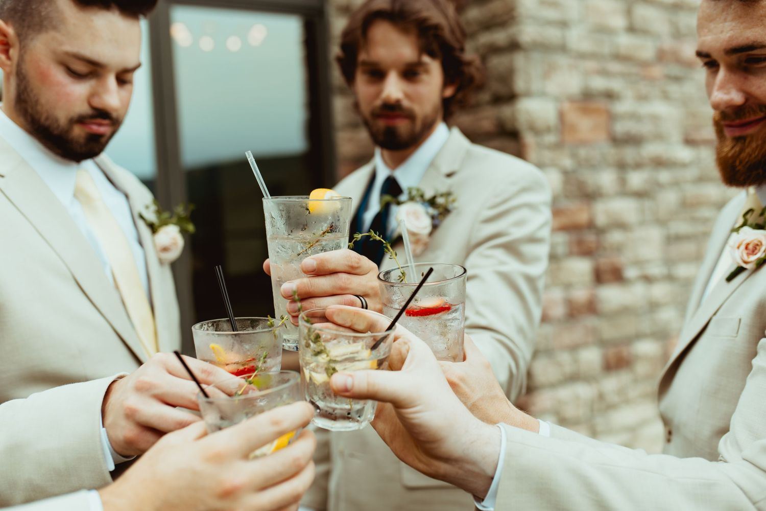 Groomsmen in tan suits toasting with cocktails at a wedding reception outdoor celebration.