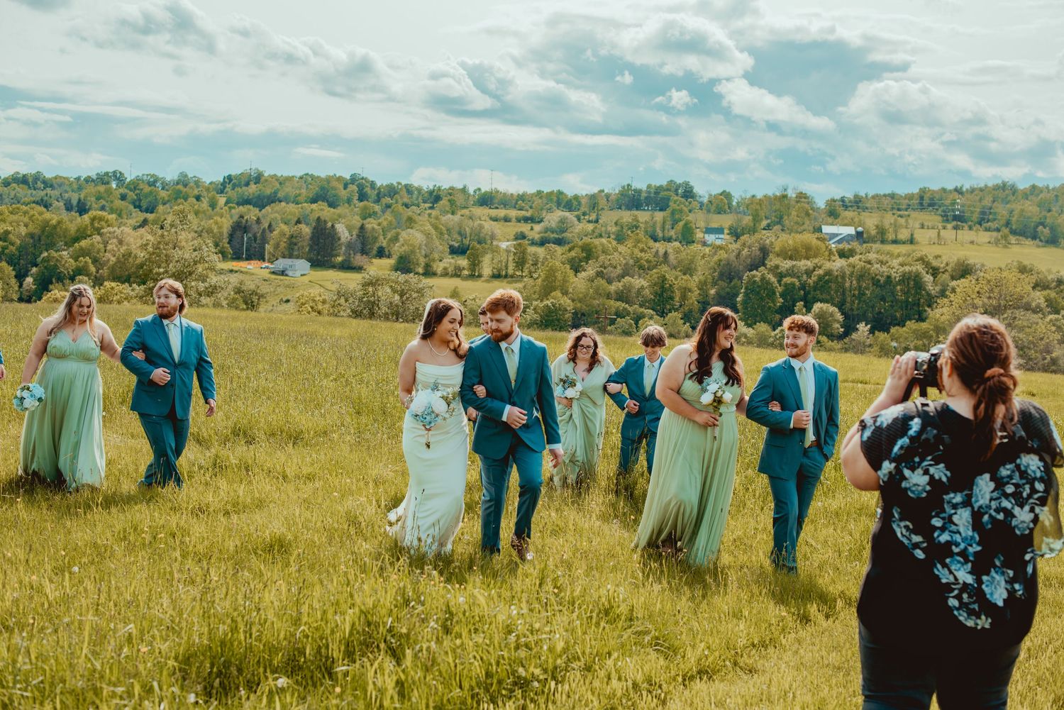 Wedding party walking through a sunny meadow with rolling hills in the background.