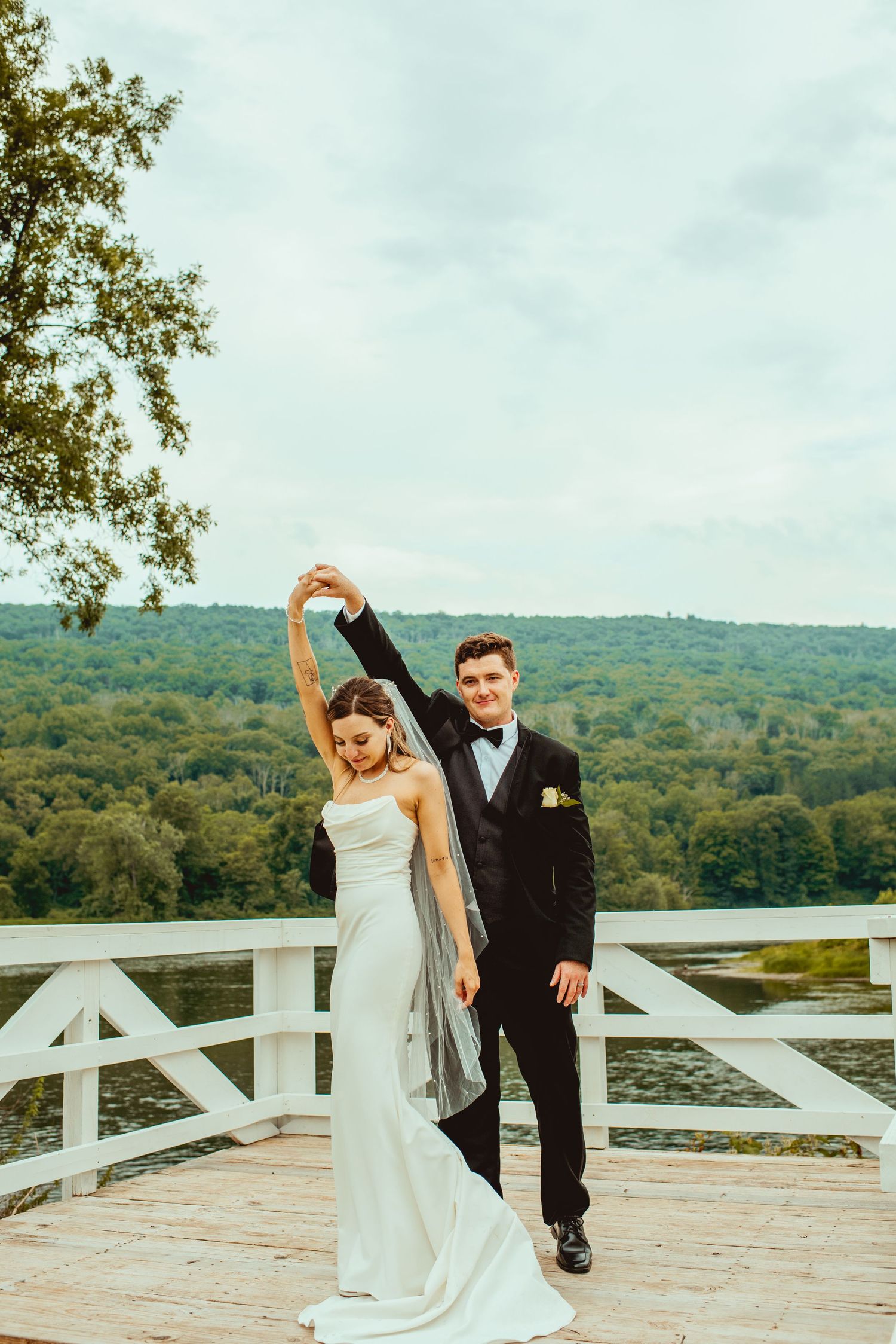 Couple dancing on white deck overlooking mountain landscape at outdoor wedding venue.