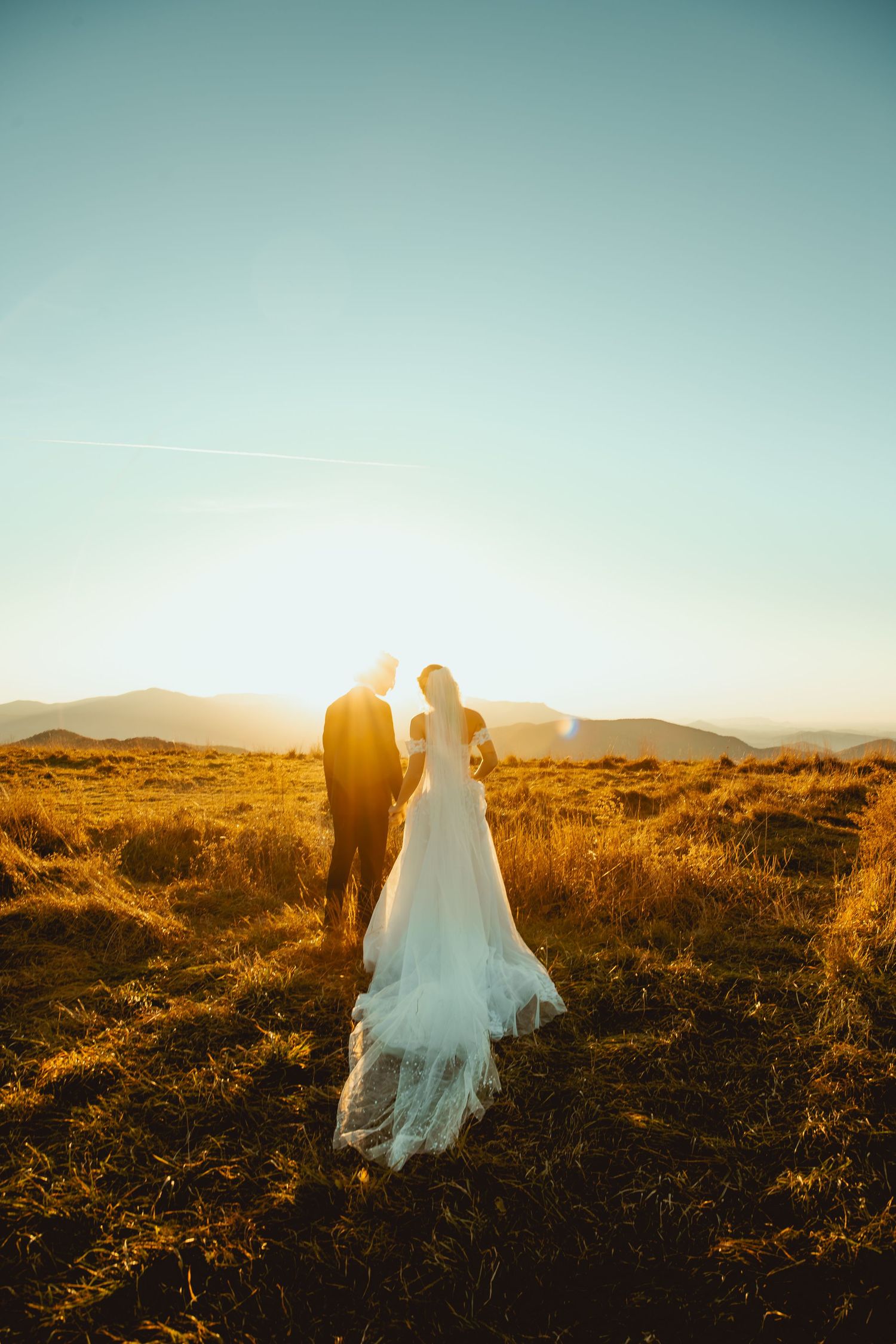 Silhouette of a wedding couple walking in golden sunlight across a mountain landscape.