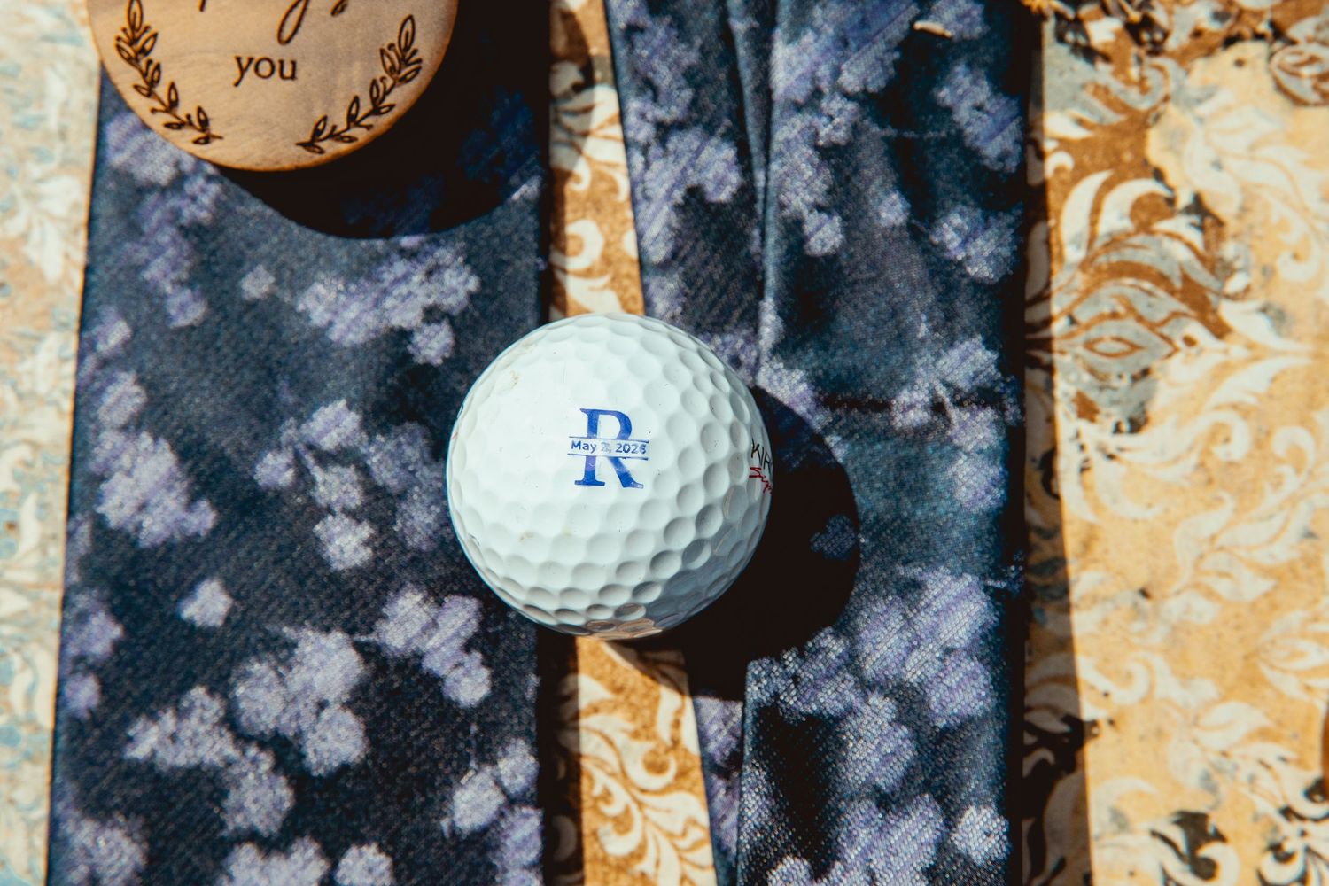 White golf ball with monogram RV resting on floral patterned ties with wooden keepsake in background.