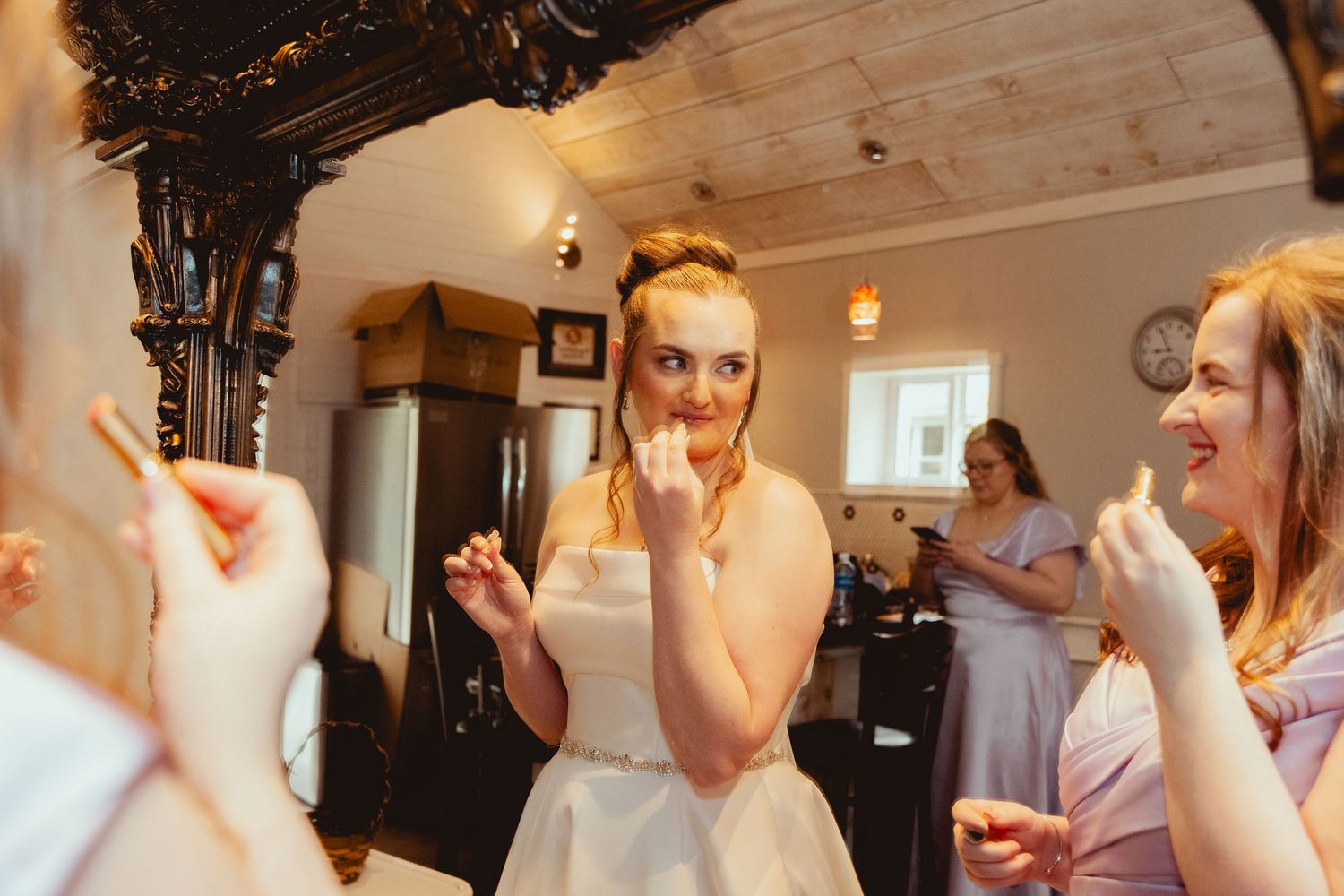 Bride in white strapless dress admiring wedding ring with smiling bridesmaids in pink dresses nearby.