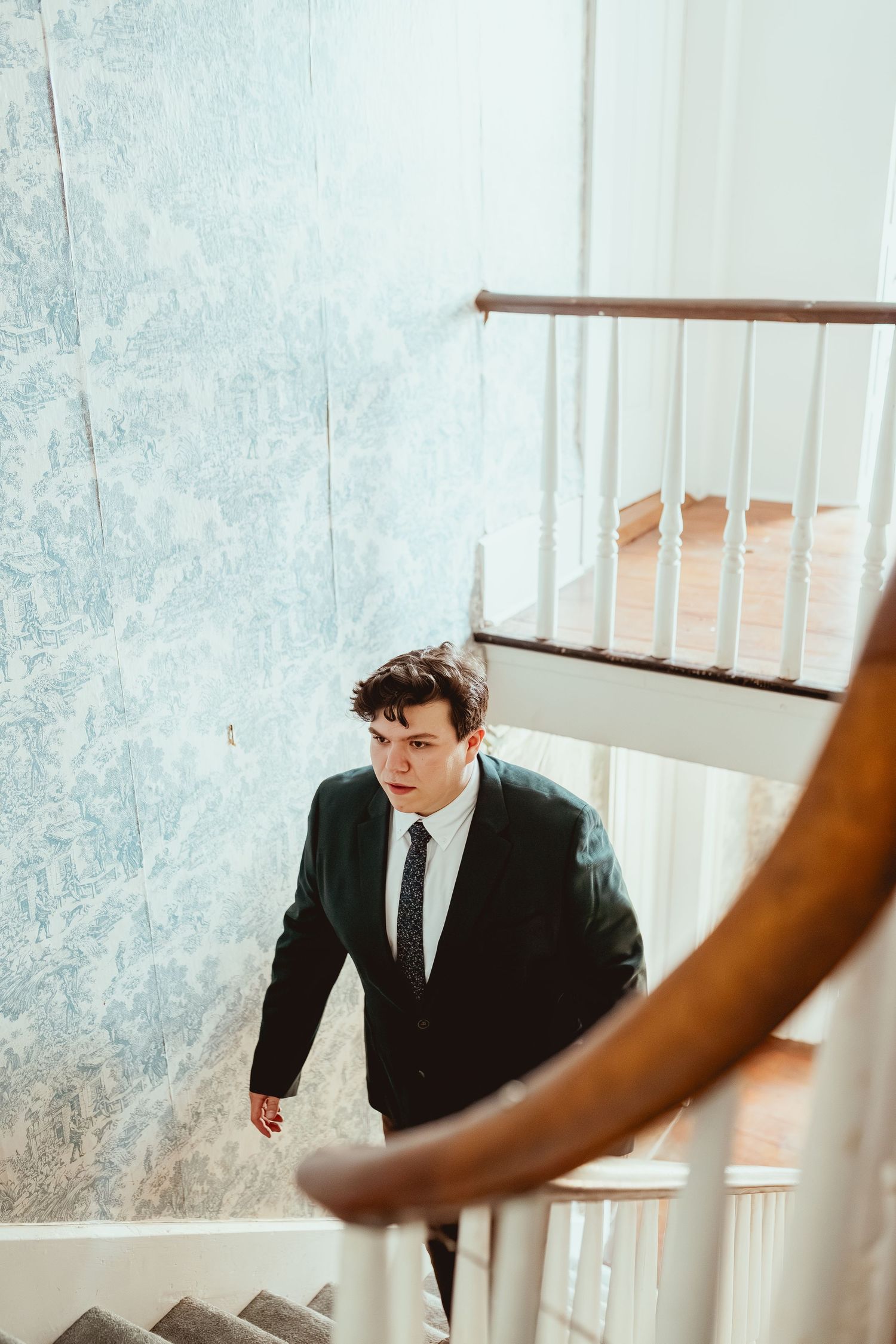 A couple in formal attire standing near a bright window with a handrail in a light-filled interior space.