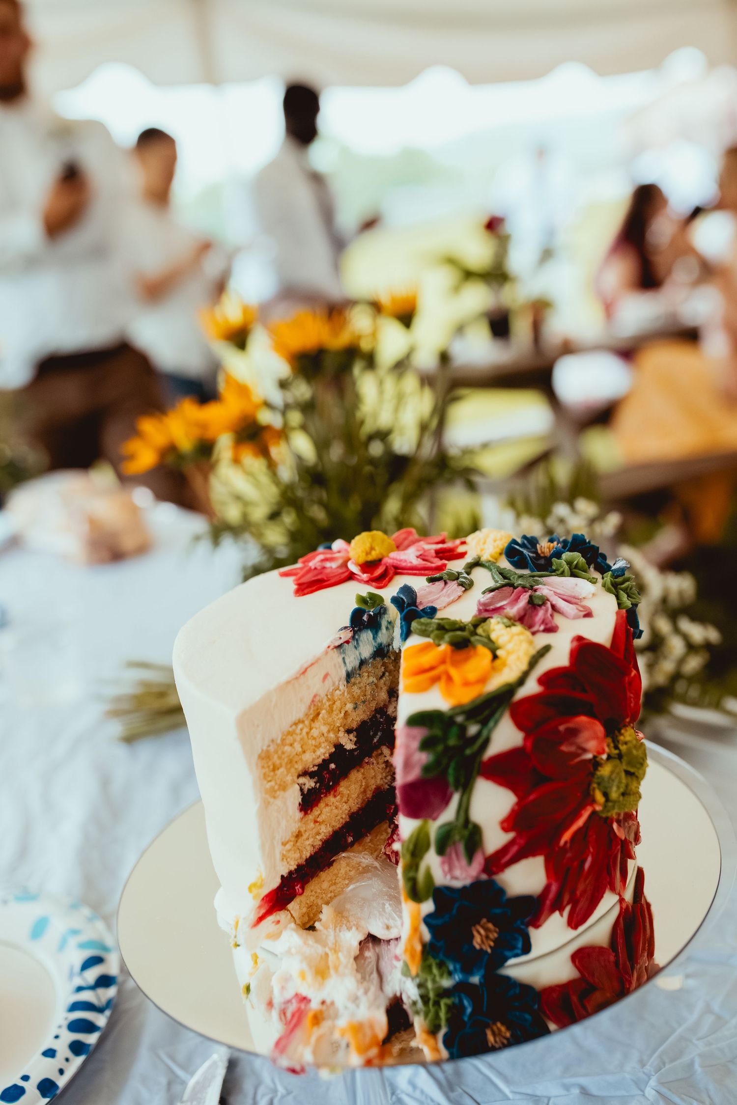 Colorful wedding cake slices decorated with vibrant flowers displayed on white plates at a reception.