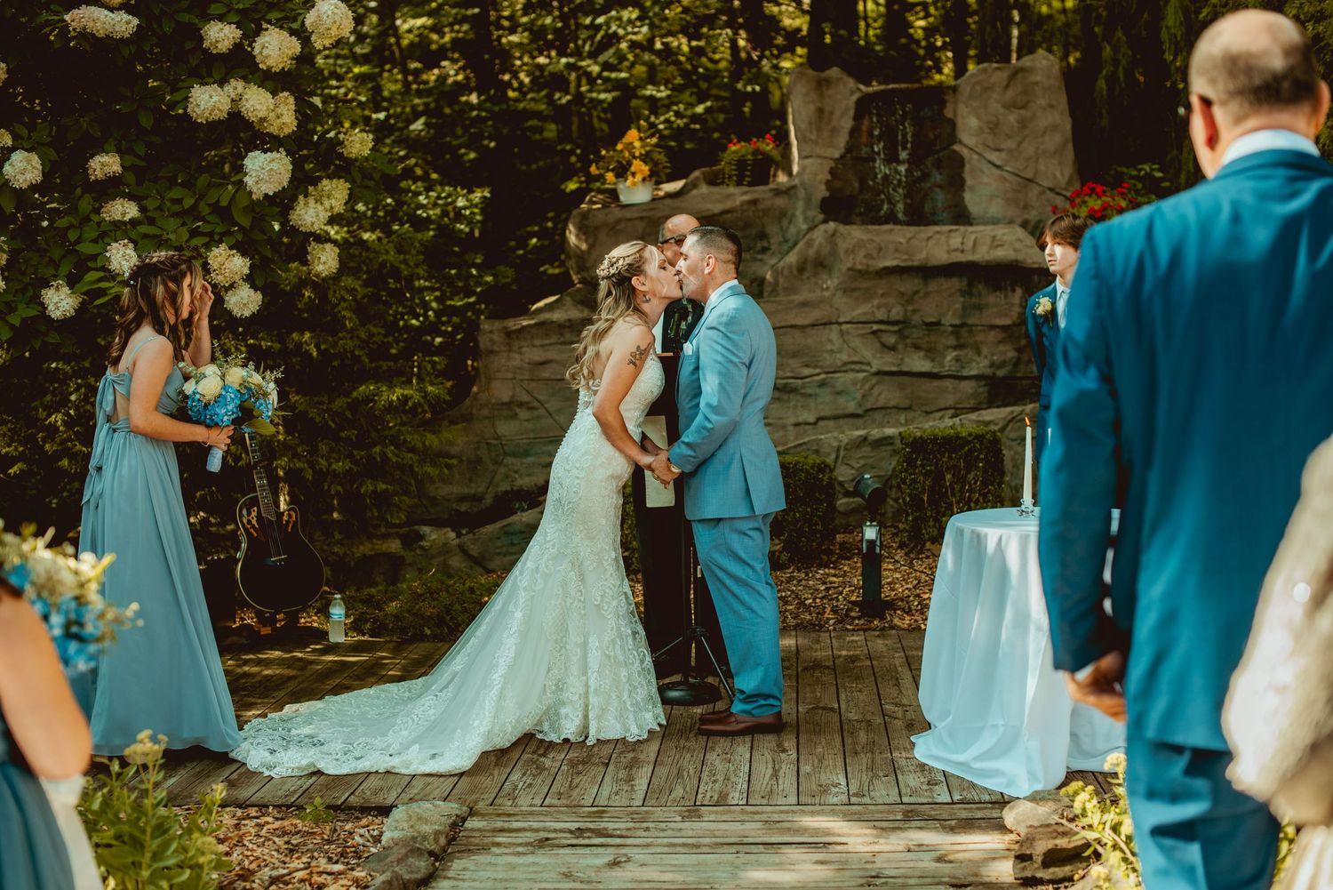 Wedding party members in turquoise dresses and suits dance together during an outdoor celebration.