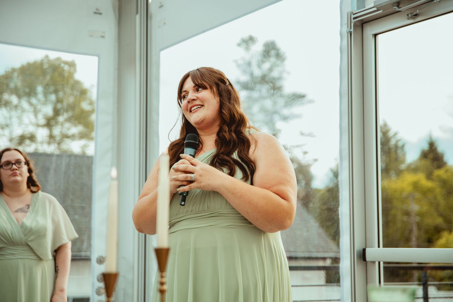 Bridesmaids in sage green dresses enjoying drinks at outdoor wedding venue.