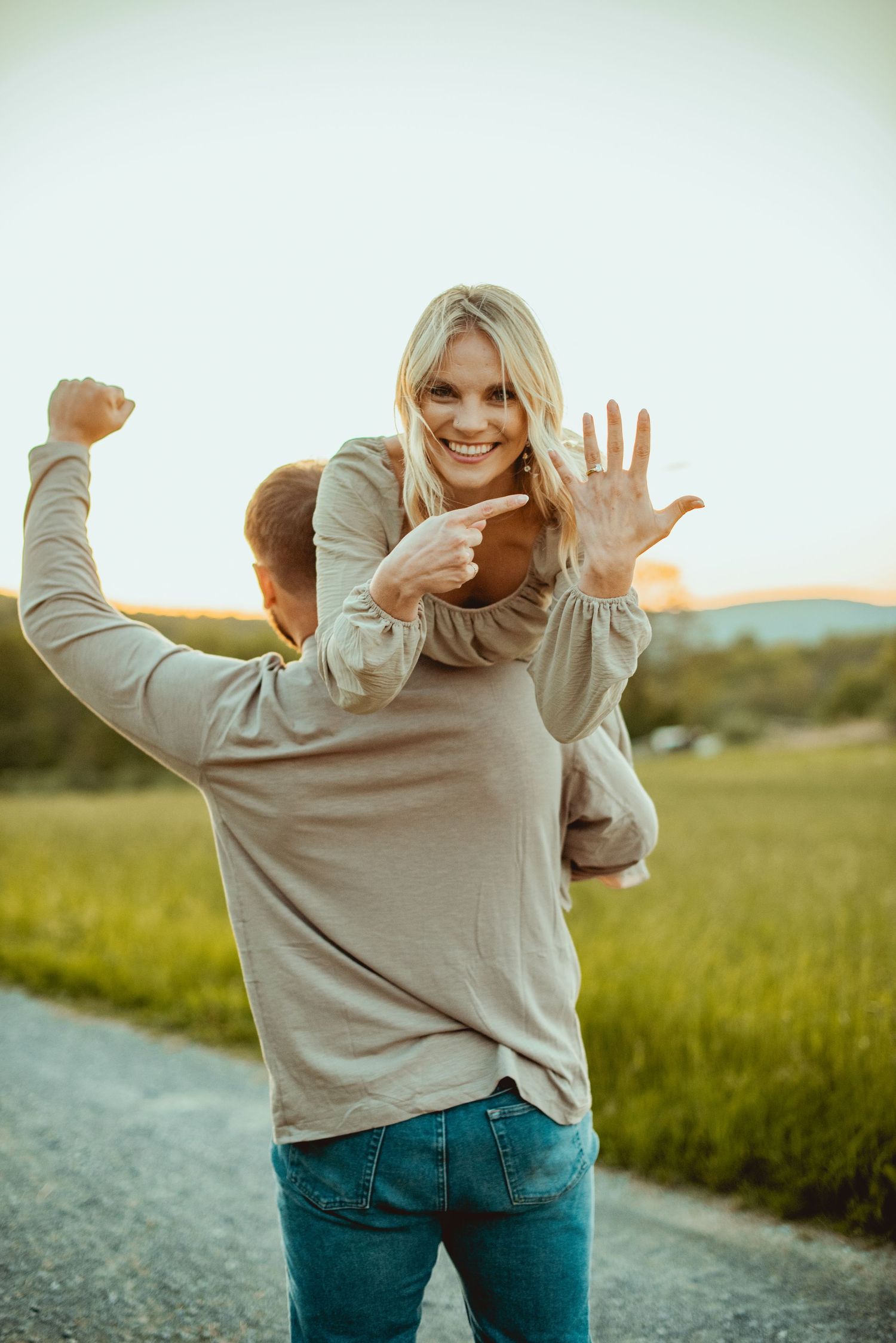Playful person in beige sweater and jeans dances joyfully on a country path at dusk.